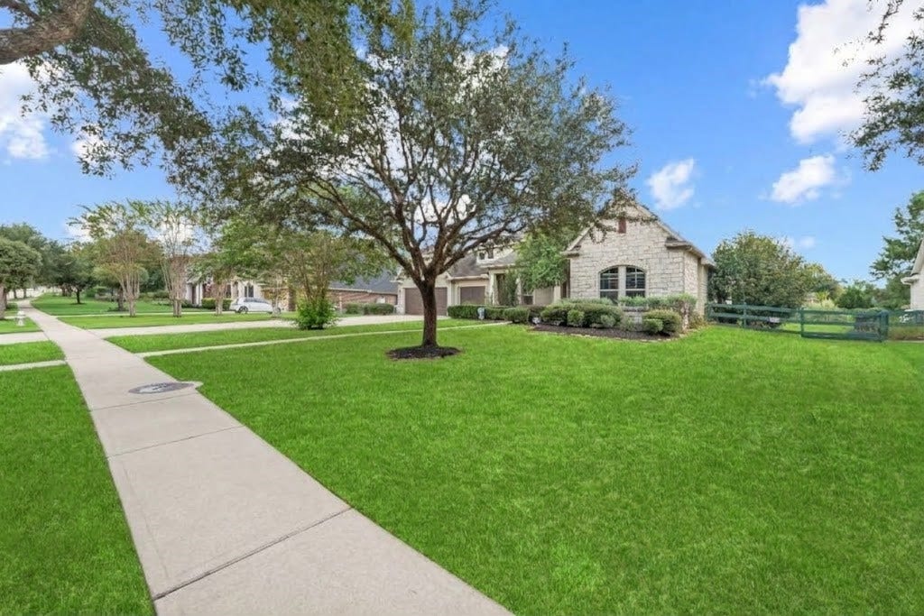 5414 Lake Hill Farm Way, Fulshear, TX 77441 View of the side lawn and front walkway, showing the property's corner lot layout, stone facade accent, low post-and-rail fencing, and lush grass lawns.