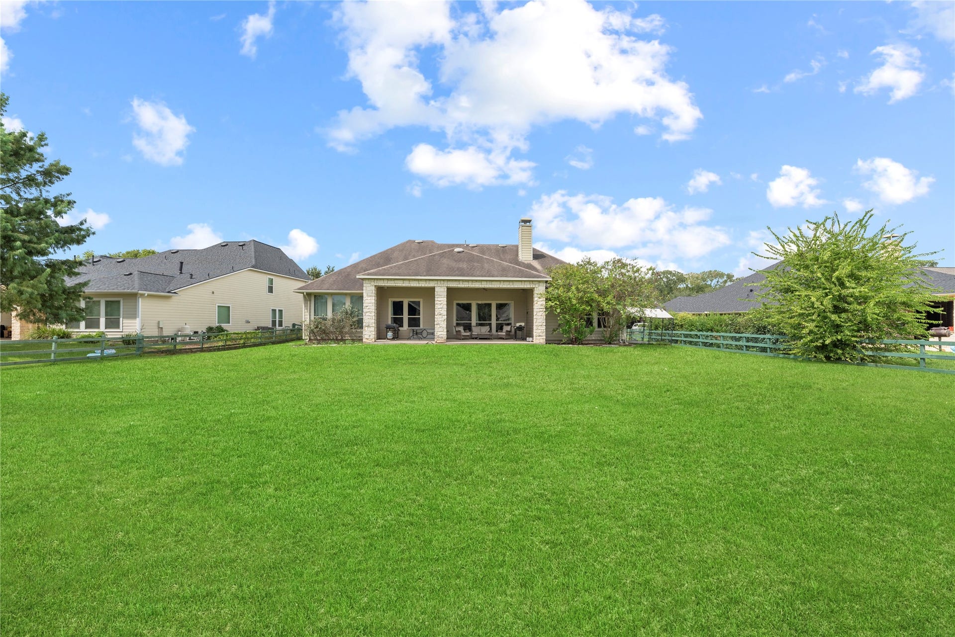 5414 Lake Hill Farm Way, Fulshear, TX 77441 Direct perspective of the home's rear exterior featuring stone column supports for the large covered porch, stone facade details, multiple rear windows, and a wide, sprawling lawn.