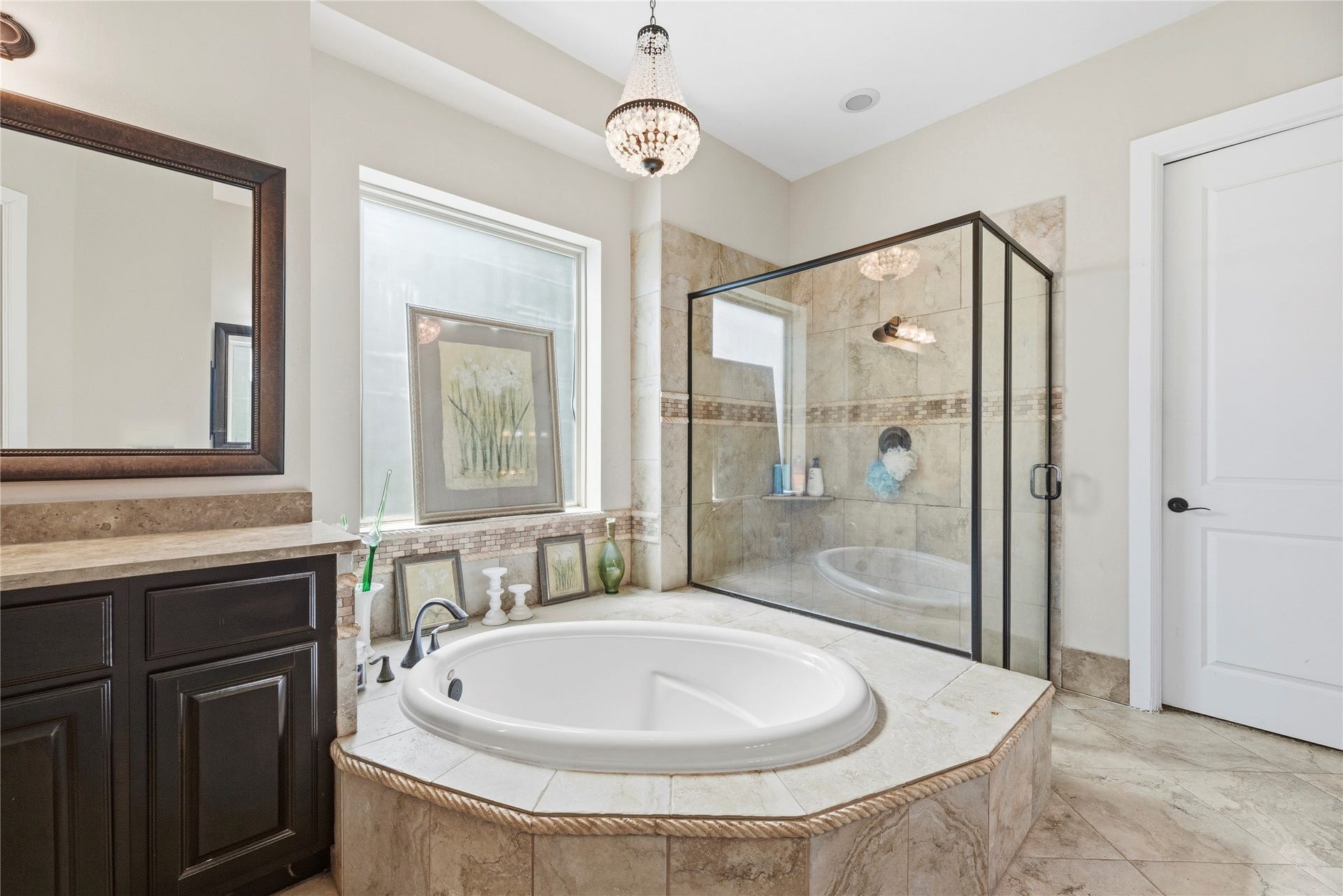 5414 Lake Hill Farm Way, Fulshear, TX 77441 Primary bathroom layout highlighting the central drop-in octagonal soaking tub with tile surround, a crystal chandelier fixture, large frost/privacy window, glass-enclosed shower stall, and tall white paneled interior doors.