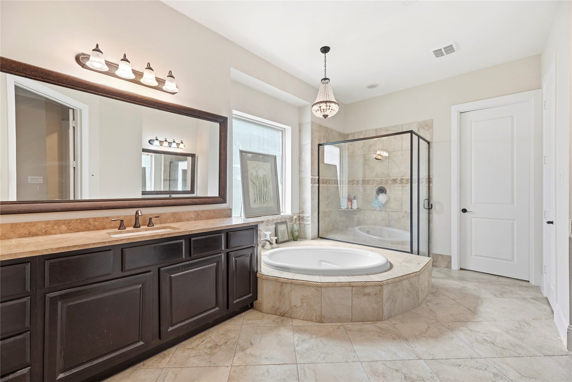 5414 Lake Hill Farm Way, Fulshear, TX 77441 Spacious primary bathroom with diagonal tile flooring, a large dark-stained double-sink vanity with beige stone/granite countertop, wall-mounted mirror with vanity bar lights, a drop-in corner soaking tub surrounded by tile, and a separate glass-enclosed walk-in shower.