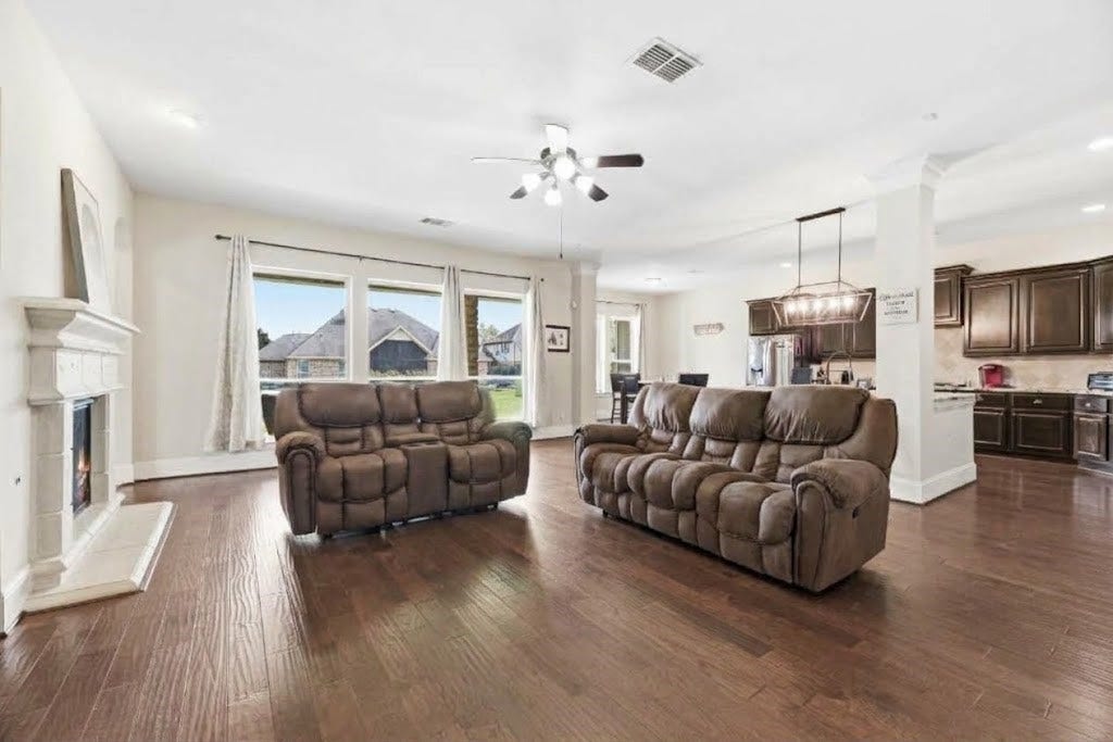 5414 Lake Hill Farm Way, Fulshear, TX 77441 Spacious living area highlighting the seamless open flow into the kitchen and breakfast nook, complete with dark wood-look floors, a gas fireplace, crown molding, and wide window openings.