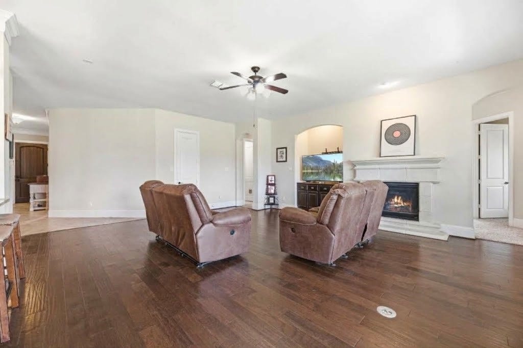 5414 Lake Hill Farm Way, Fulshear, TX 77441 Angle of the living room showing the central gas fireplace, high ceilings with ceiling fan, dark wood-look floor, and wide archways connecting to the main entry hallway and media area.