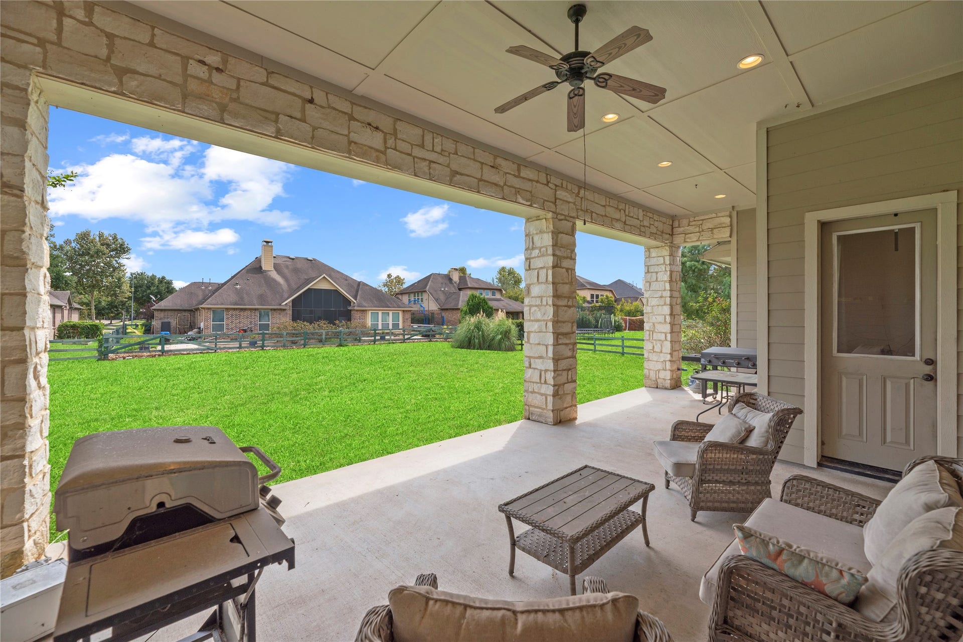 5414 Lake Hill Farm Way, Fulshear, TX 77441 Large covered rear patio featuring stone support pillars, outdoor ceiling fan with lighting, recessed lights, concrete flooring, exterior doorway, and direct open view to the backyard.