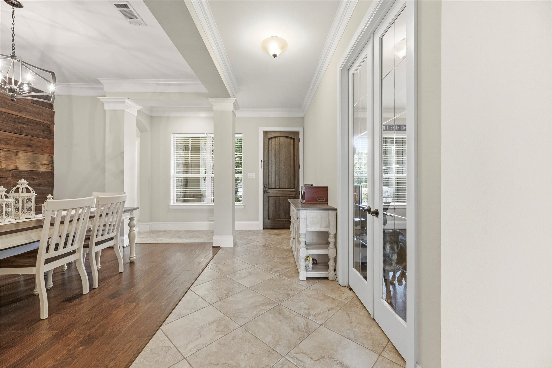 5414 Lake Hill Farm Way, Fulshear, TX 77441 Long hall featuring diagonal tile flooring, recessed light, glass-pane French doors leading into a study/office, and an open sightline to the formal dining area with wood-look flooring, accent columns, and a rustic wood accent wall.