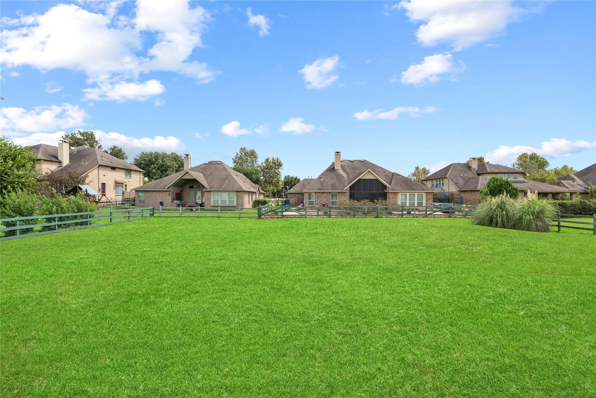 5414 Lake Hill Farm Way, Fulshear, TX 77441 Overview of the broad, flat grass backyard bounded by a green post-and-rail fence, offering expansive lawn space and clear sightlines to neighboring properties.