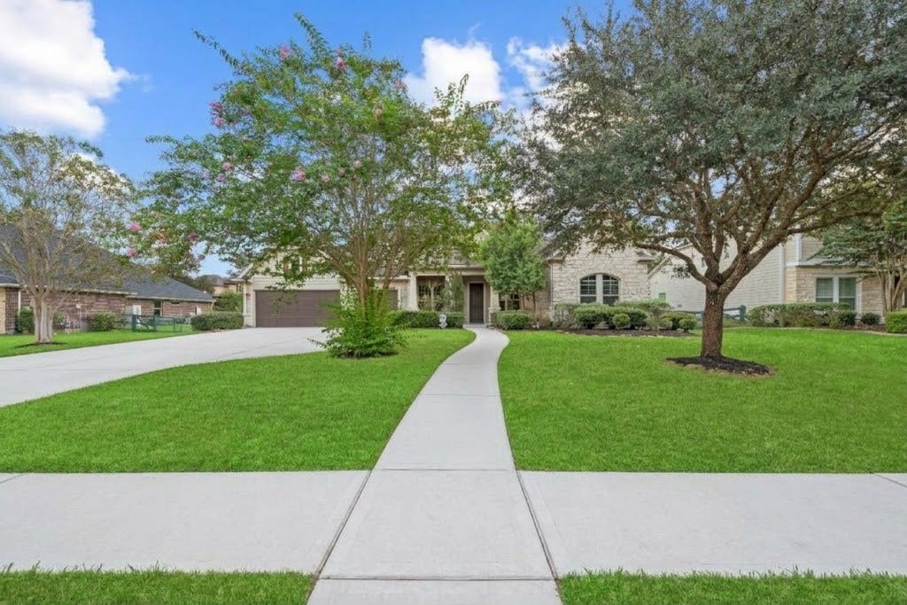 5414 Lake Hill Farm Way, Fulshear, TX 77441 Straight-on perspective from the front sidewalk featuring a central concrete walkway leading to the covered front entry, flanked by lush green lawns, shade trees, and mature landscaping.