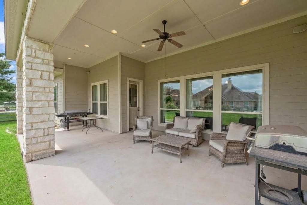 5414 Lake Hill Farm Way, Fulshear, TX 77441 Extended view of the covered back patio highlighting stone columns, recessed lighting, ceiling fan, wide window openings along the home's rear wall, and concrete deck space.