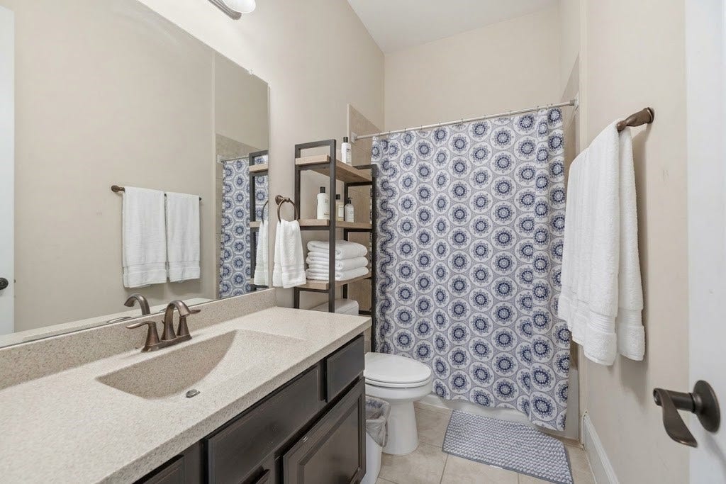 5414 Lake Hill Farm Way, Fulshear, TX 77441 Full bathroom complete with a dark wood vanity, solid-surface countertop with integrated sink, full-length wall mirror, tile floor, and a tub/shower combination with a tiled surround.