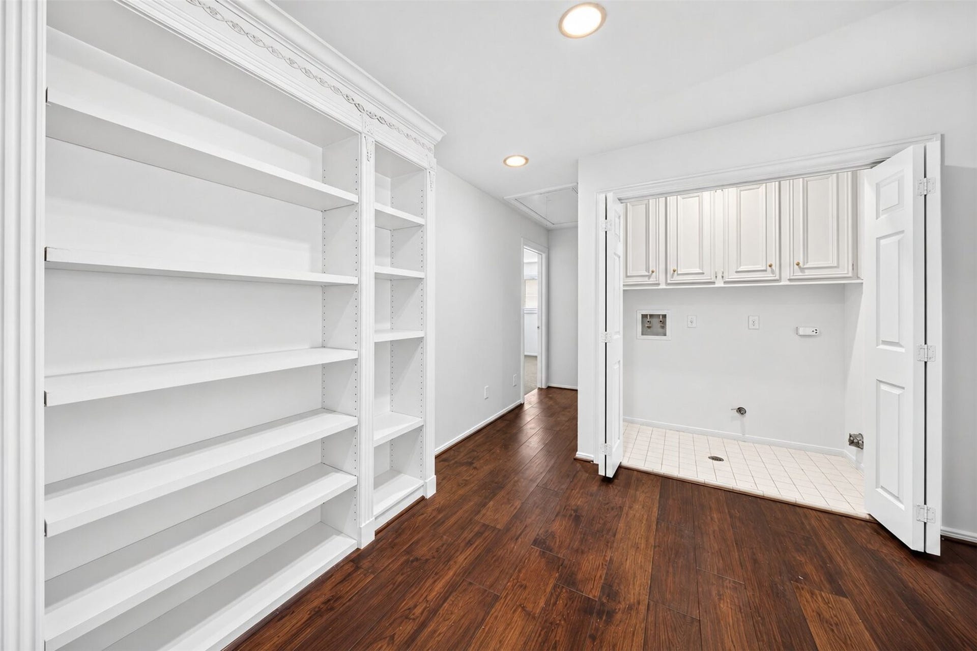 Built-in shelving lines the upstairs hall beside a laundry alcove with overhead cabinets.