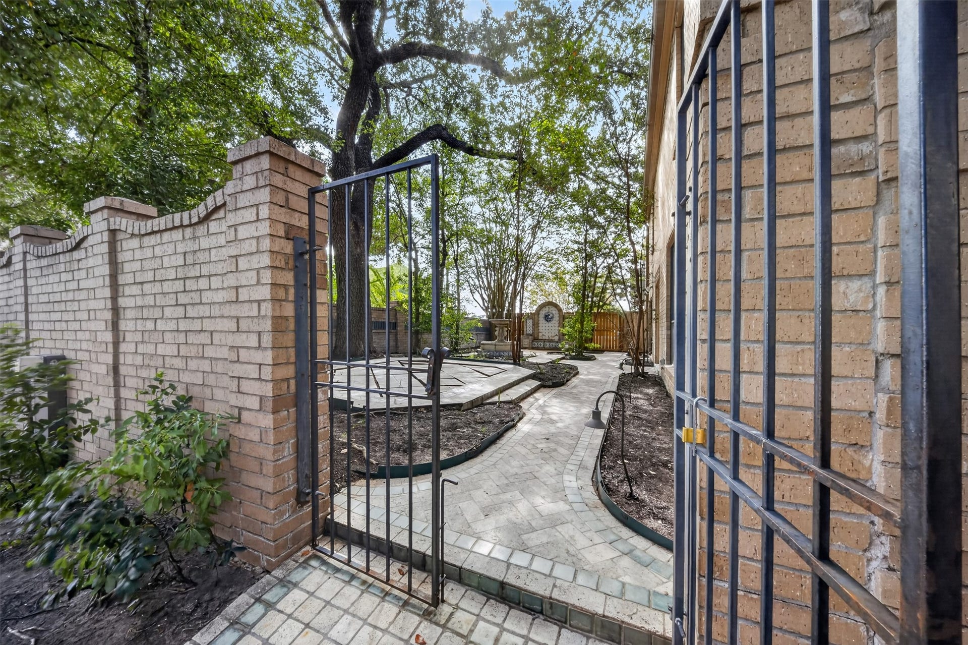 Metal courtyard gate opens to a paved garden path beside the brick home.