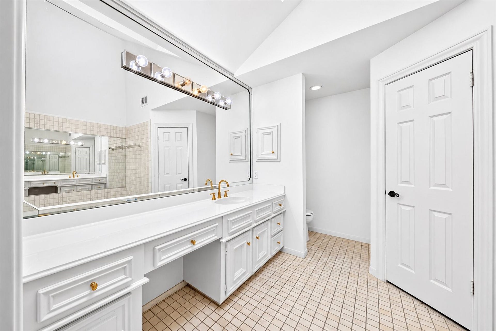 Long bathroom vanity with white cabinetry, a seated counter area and a broad mirror.