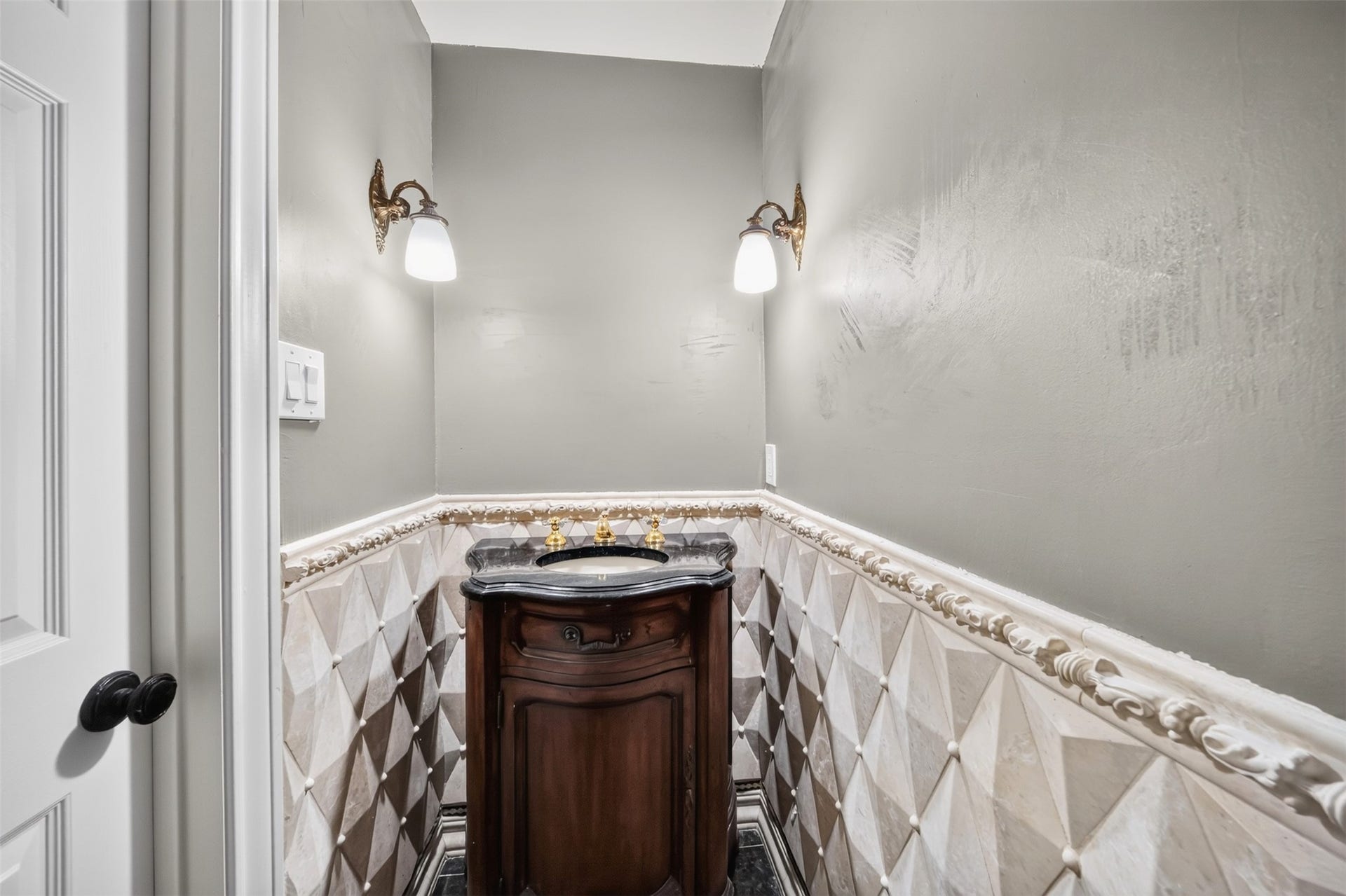 Powder room with a furniture-style vanity, wall sconces and patterned wall tile.