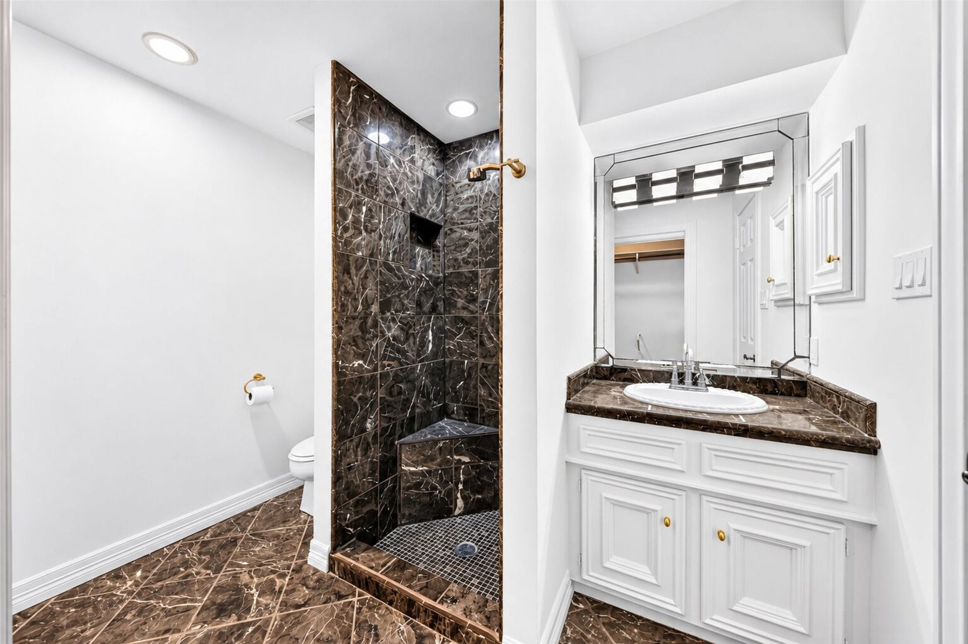 Bathroom with a white vanity and an open shower finished in dark veined tile.