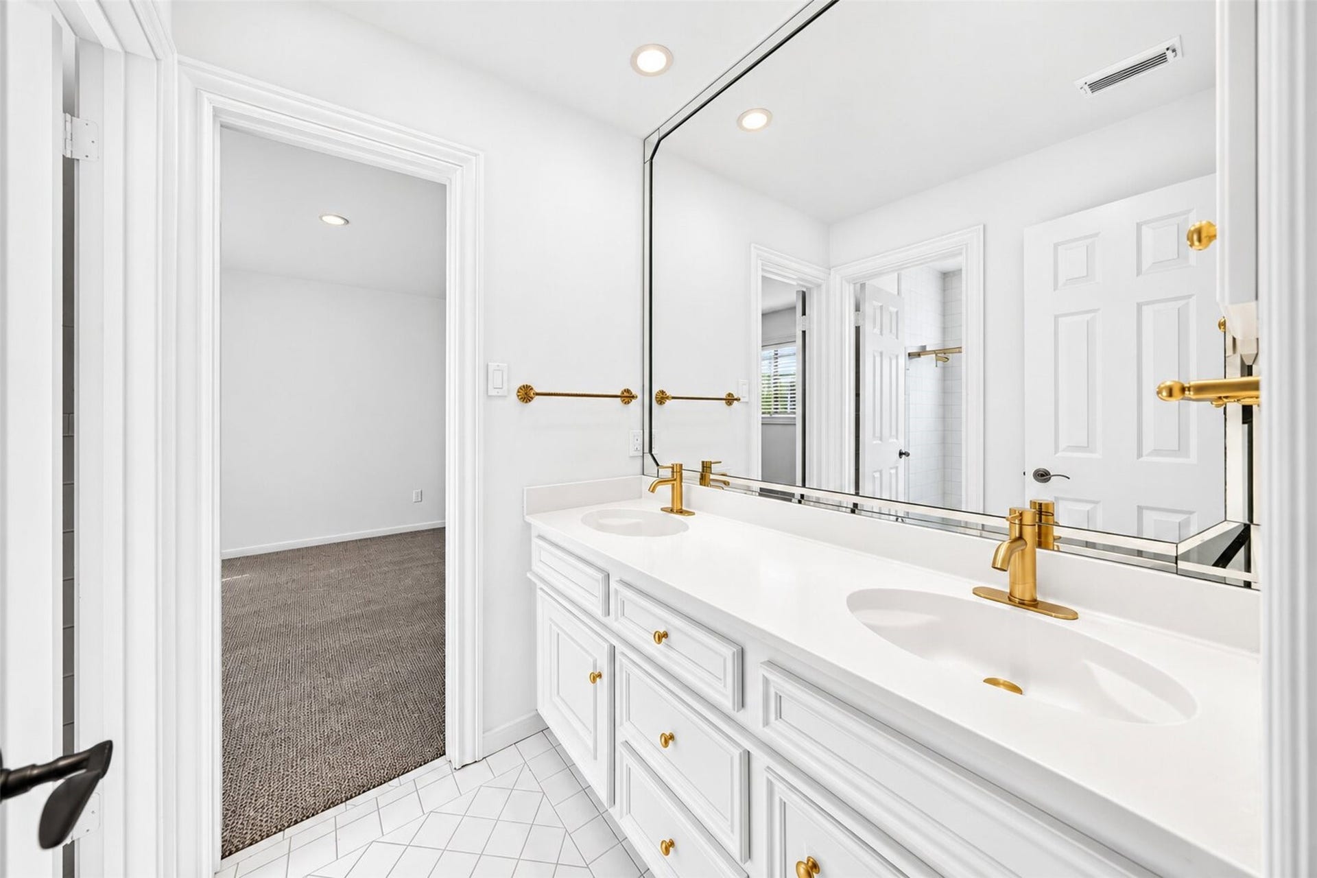 Double-sink vanity with white cabinetry, gold-tone faucets and a wide mirror.