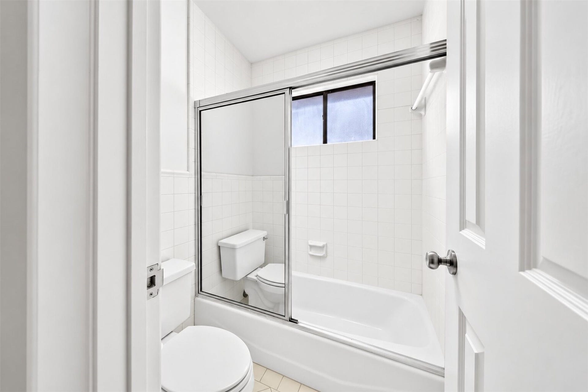 Tub and shower combination with sliding glass doors, white tile and a high window.