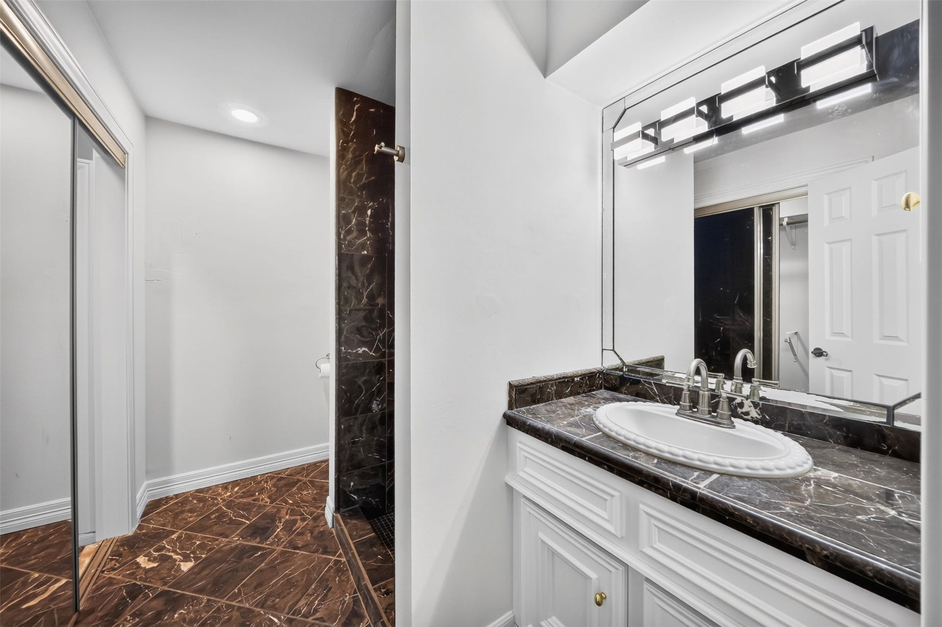 Bathroom vanity with an oval basin, dark counter and mirrored closet doors nearby.