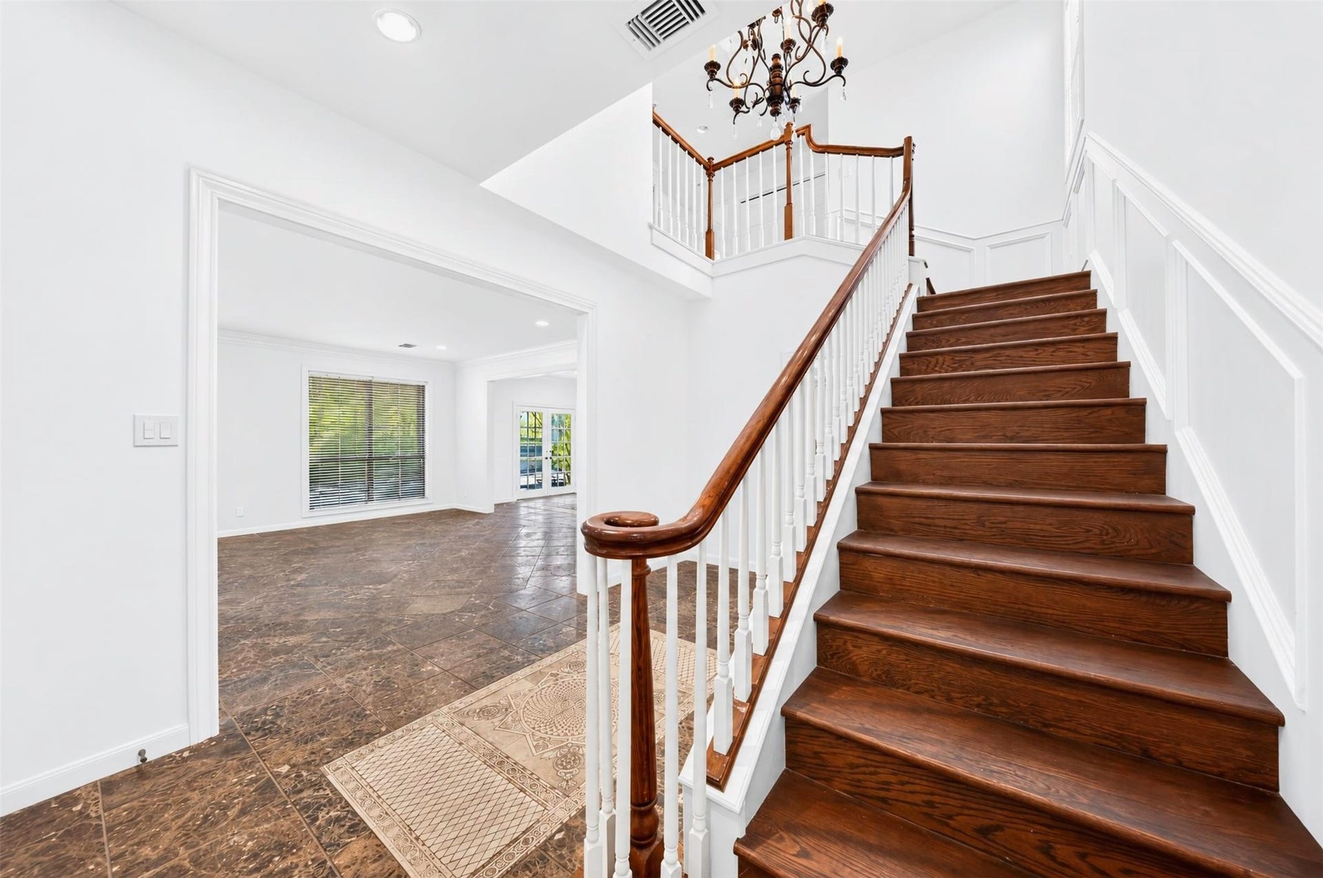 Open foyer with a wood staircase, white balusters and a chandelier above.