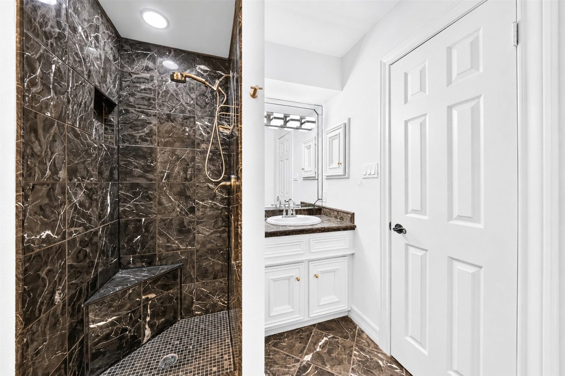 Dark-tiled shower with a built-in bench, recessed niche and handheld fixture.
