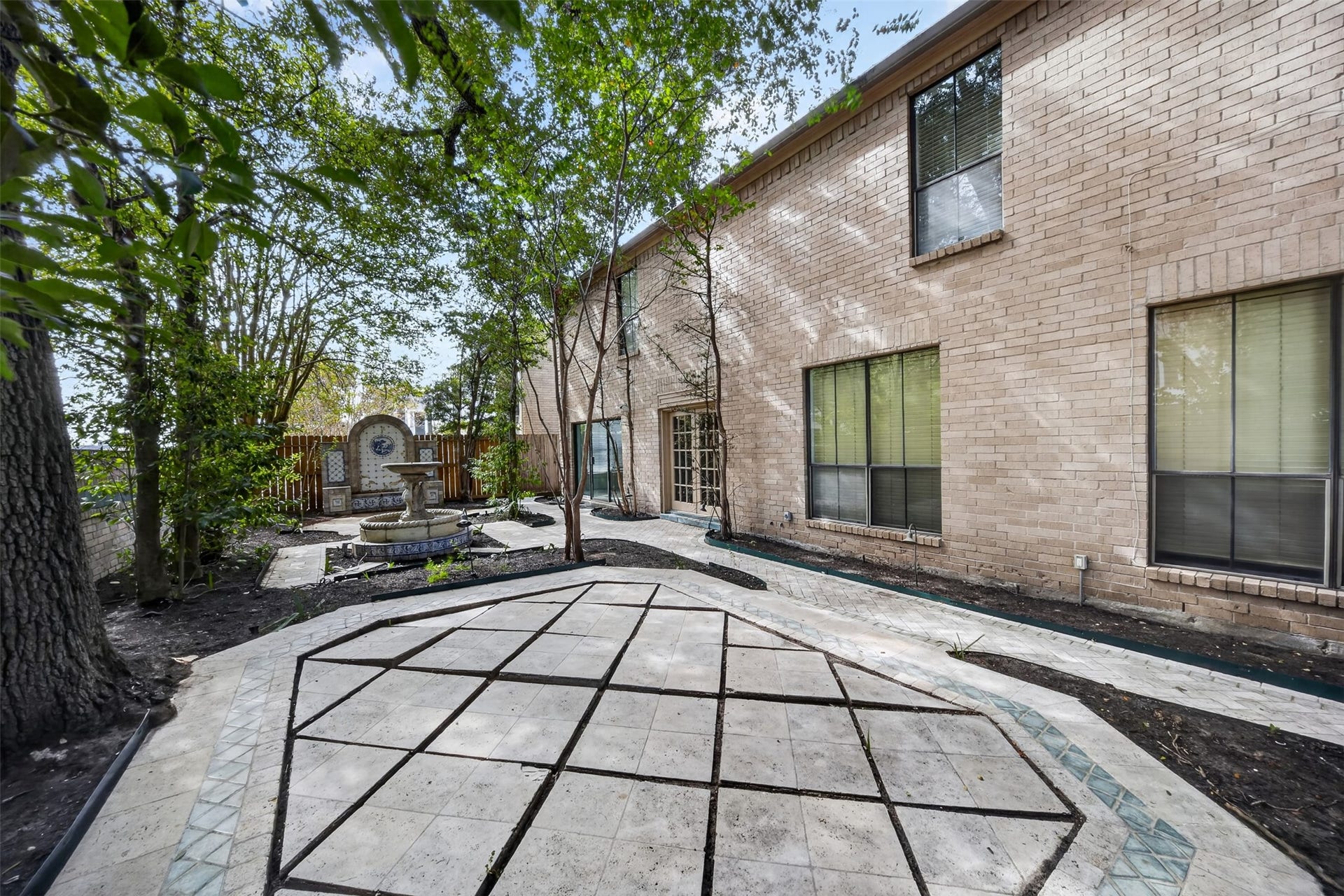 Courtyard with geometric paving, mature trees and a decorative fountain beside the brick exterior.