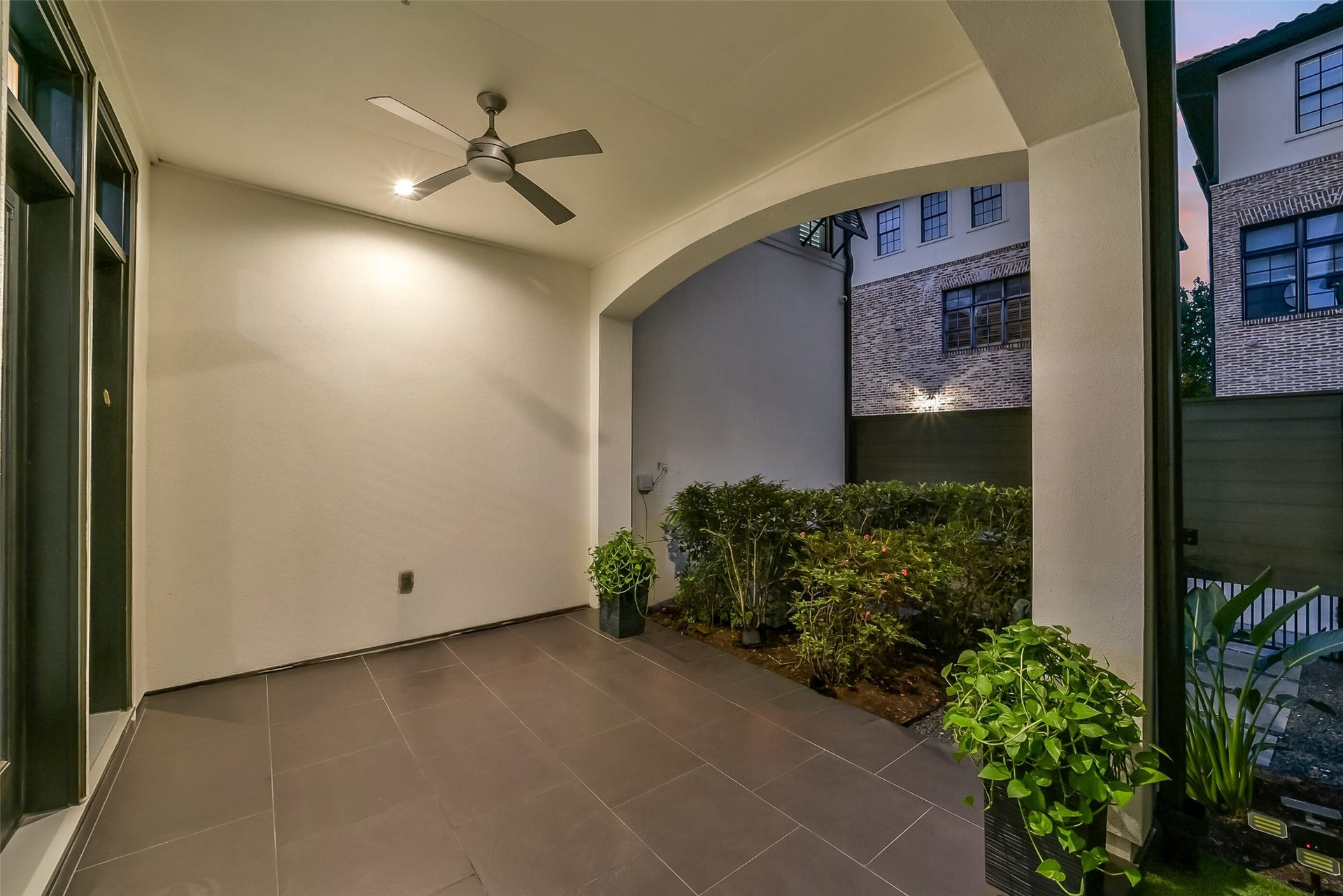11 Southside Circle, Southside Place, TX 77025 Private covered patio with an arched opening, ceiling fan, and large-format tile flooring, ideal for outdoor dining or relaxing year-round. Lush landscaping and a fenced courtyard setting add privacy, with French doors connecting seamlessly to the main living area.