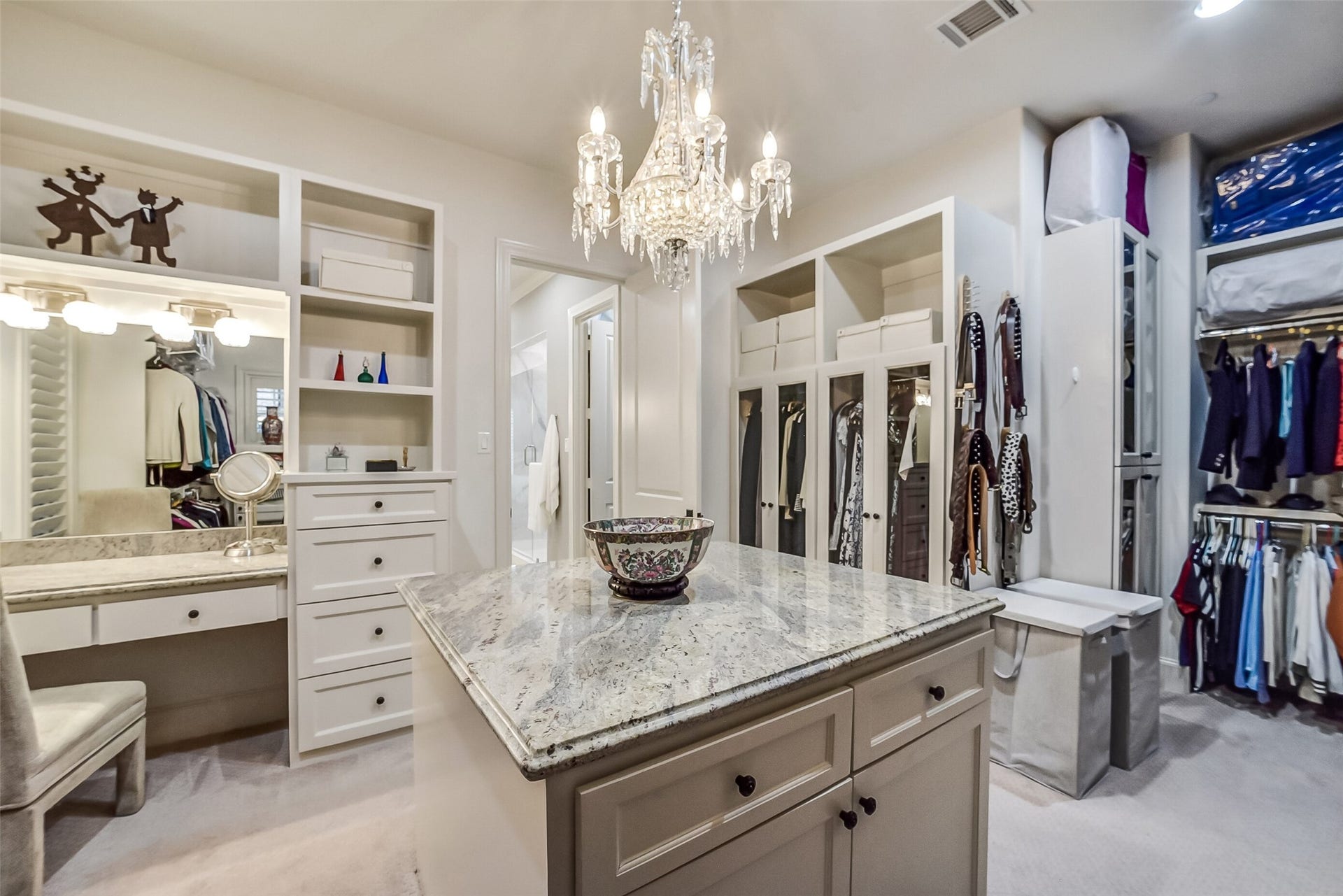 11 Southside Circle, Southside Place, TX 77025 One of two expansive walk-in closets offers an exceptional blend of luxury and functionality. A generous center island, custom built-ins, and hanging space provide additional storage and a convenient space for wardrobe planning and organization. A dedicated vanity with mirror creates the perfect space for getting ready in style.