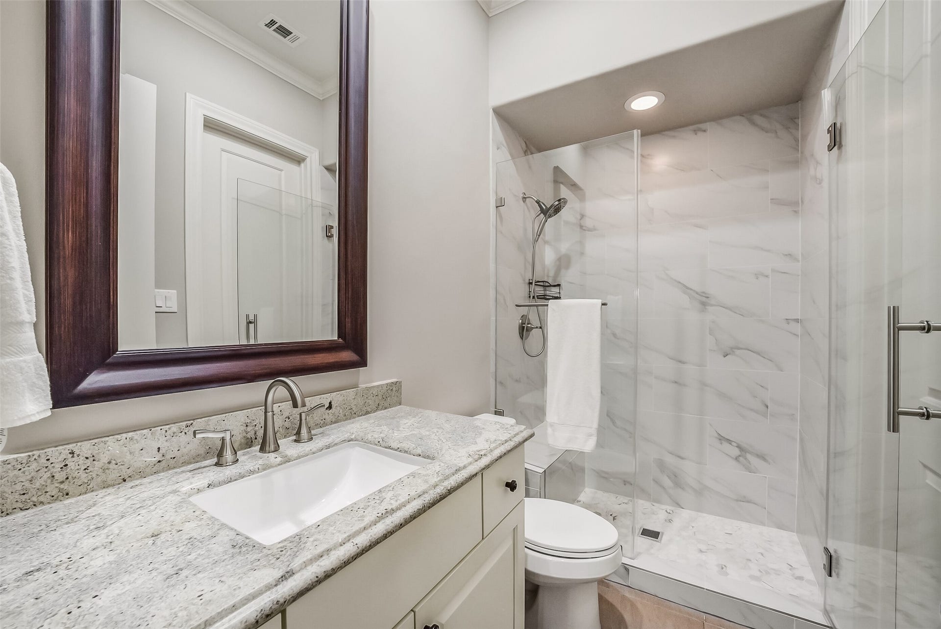 11 Southside Circle, Southside Place, TX 77025 Secondary bath with a granite-top vanity, undermount sink, and a framed mirror. The walk-in shower has a frameless glass door, marble-look tile, a built-in bench, and a handheld shower head.