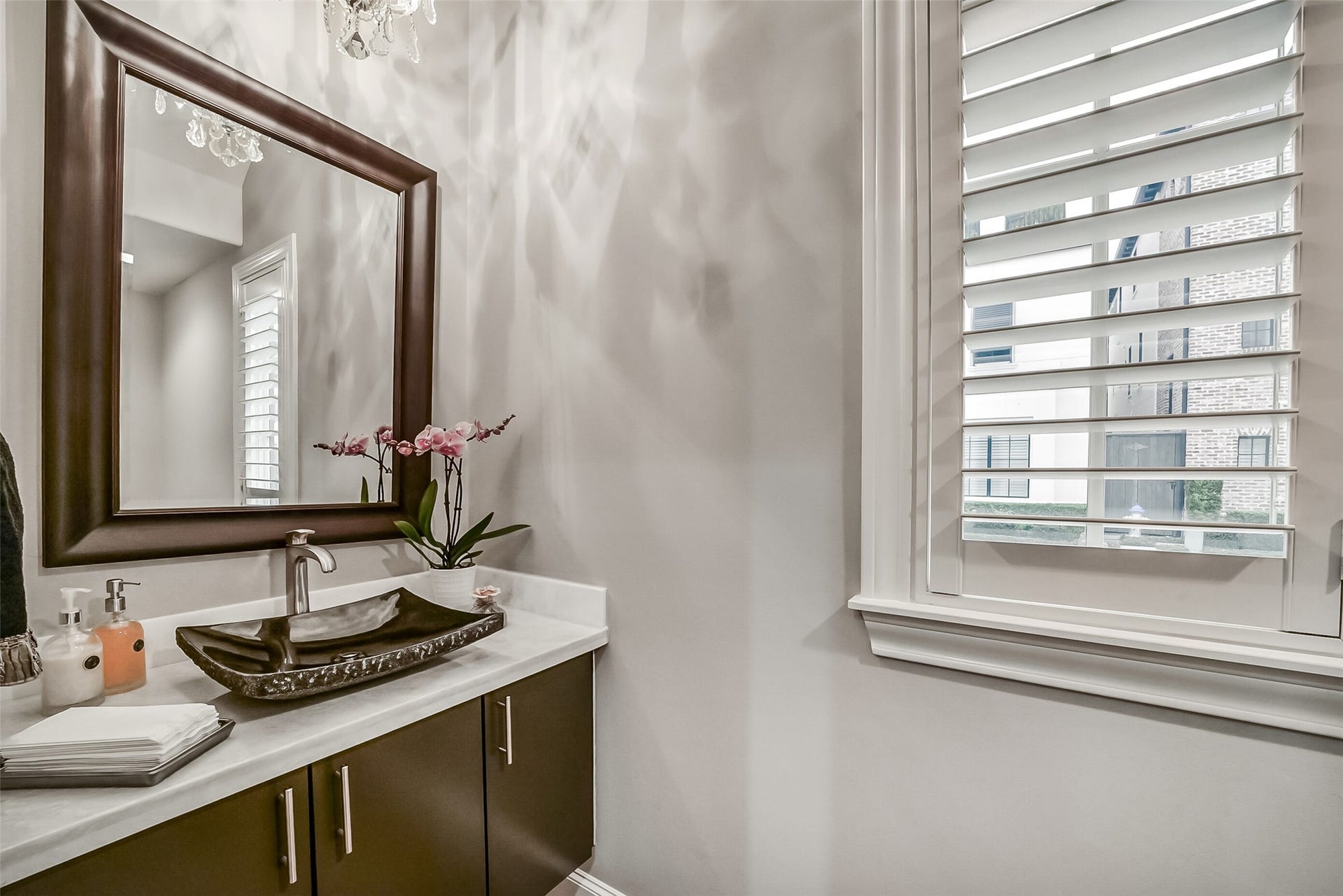 11 Southside Circle, Southside Place, TX 77025 An elegant half bath featuring a rich espresso-finished vanity, a sophisticated dark vessel sink, and crisp plantation shutters, creating a stylish and inviting space for guests.