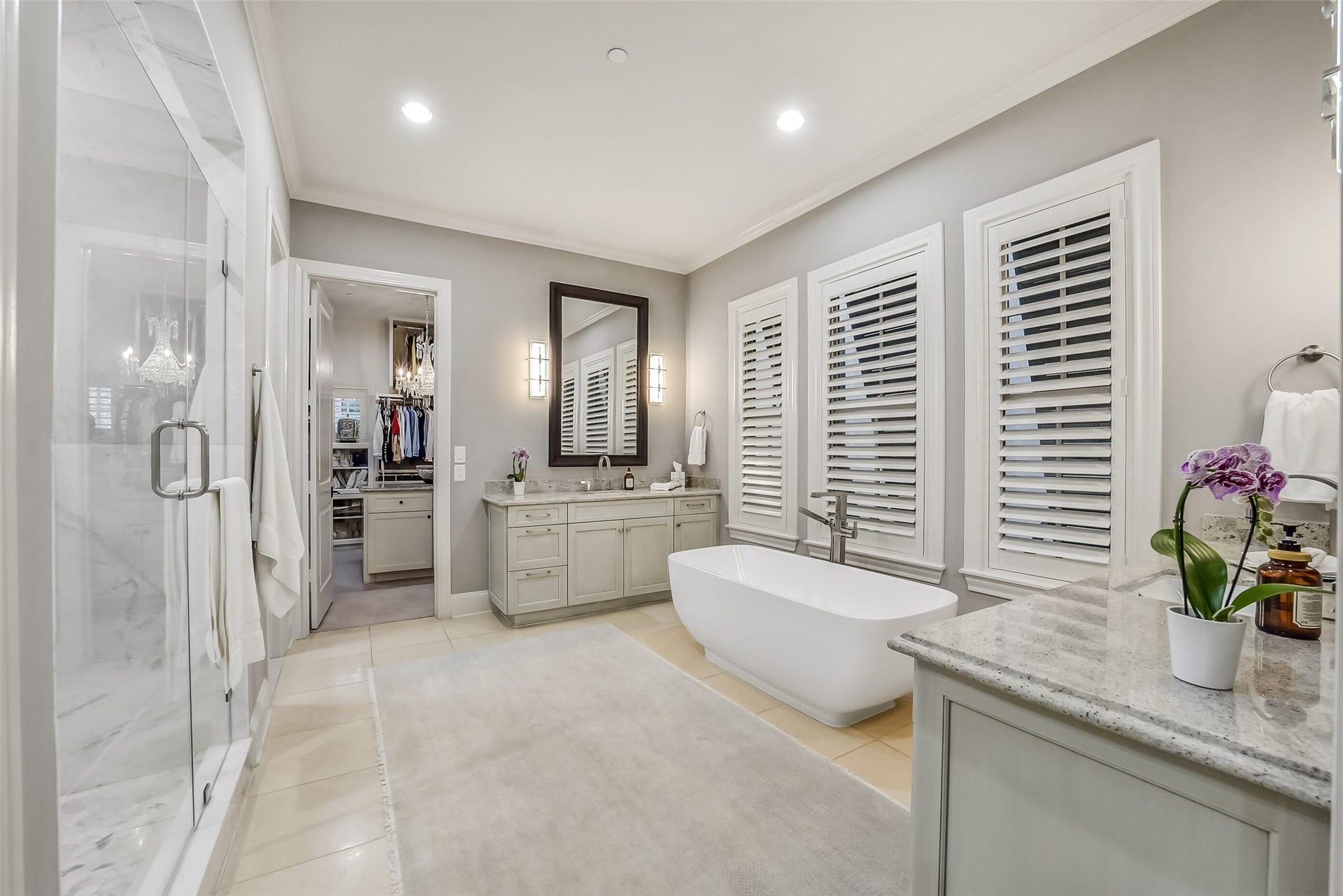 11 Southside Circle, Southside Place, TX 77025 Luxurious primary bathroom featuring two separate vanities, a modern freestanding soaking tub framed by three shuttered windows for natural light and privacy, a seamless glass-enclosed shower, and direct access to 2 spacious walk-in closets.