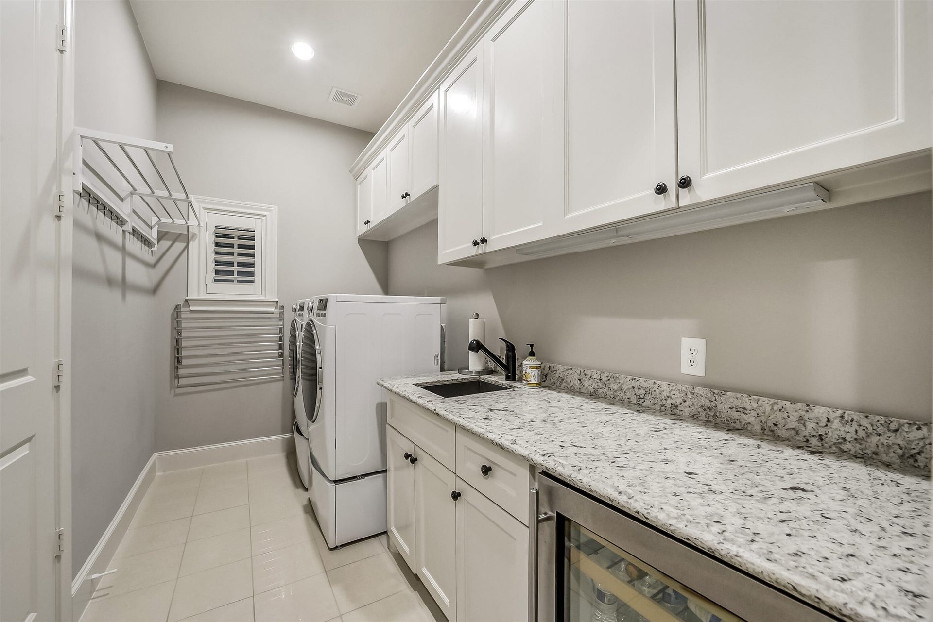 11 Southside Circle, Southside Place, TX 77025 Well-appointed utility room with white cabinetry, granite countertops, and a built-in sink. Front-loading washer and dryer sit on pedestals, and wall-mounted drying racks and under-cabinet lighting make laundry day easier. A beverage cooler adds a nice extra.