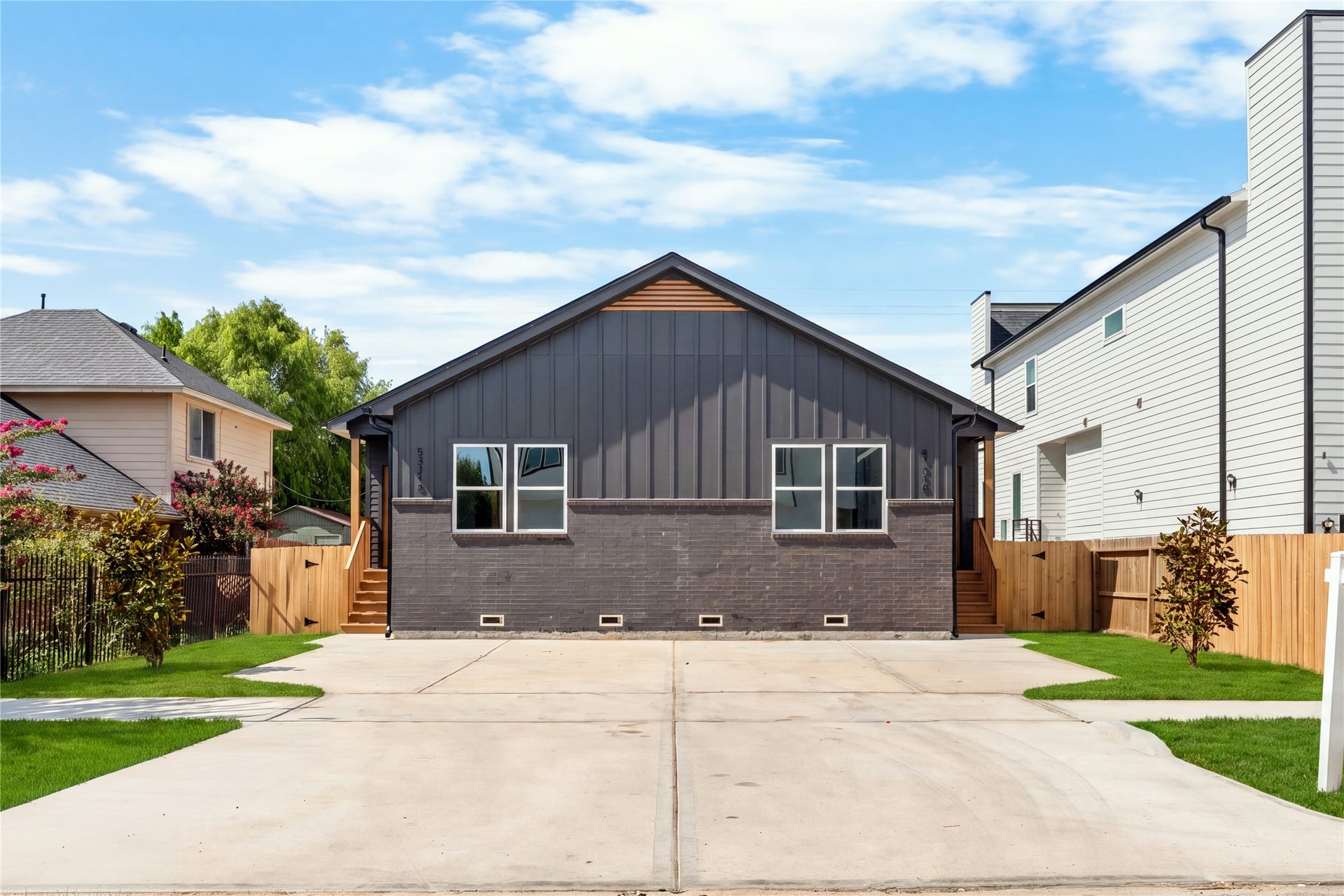 5321 Rue Street, Houston, TX 77033 Modern elevation with bold charcoal board-and-batten siding deep brick accents, double-entry wood steps, and an expansive concrete drive with ample parking space.