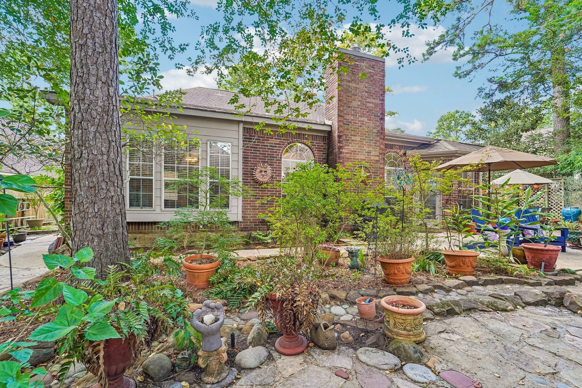 14 Serene Creek Place, The Woodlands, TX 77382 Charming backyard oasis with lush greenery, a cozy brick patio, and ample space for outdoor relaxation under the shade of mature trees.