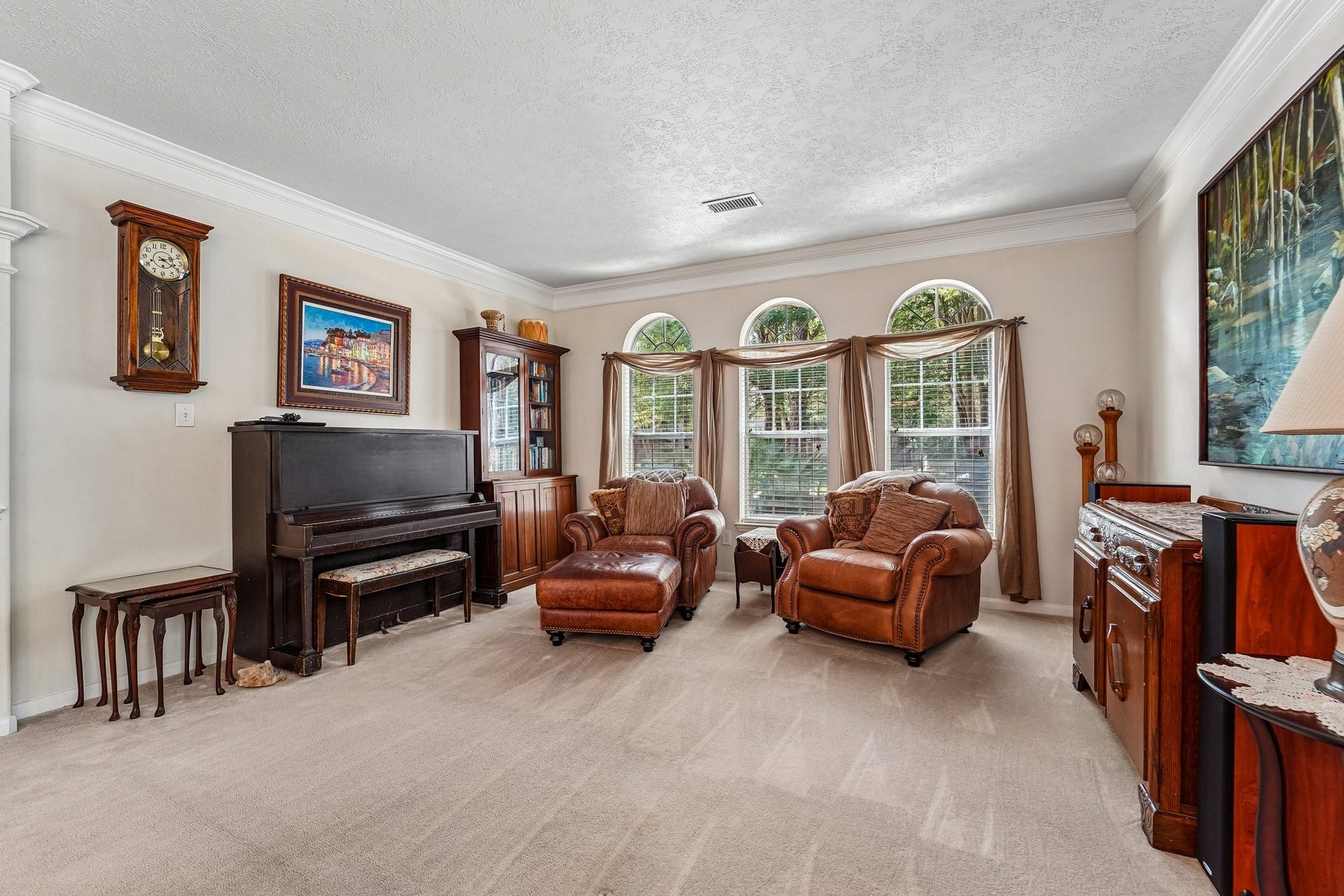 14 Serene Creek Place, The Woodlands, TX 77382 Front formal living room with large arched windows, cozy leather seating, and a charming piano - perfect for relaxation and entertainment.