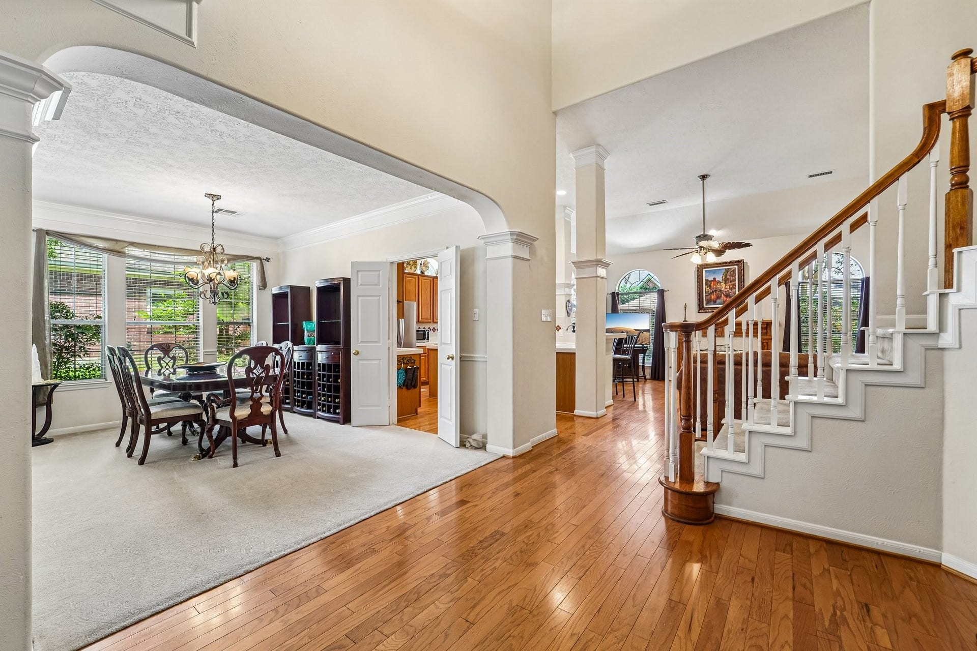 14 Serene Creek Place, The Woodlands, TX 77382 Elegant open-concept living space featuring a formal dining area with large windows, rich wood flooring, and a grand staircase, seamlessly connecting to the family room.