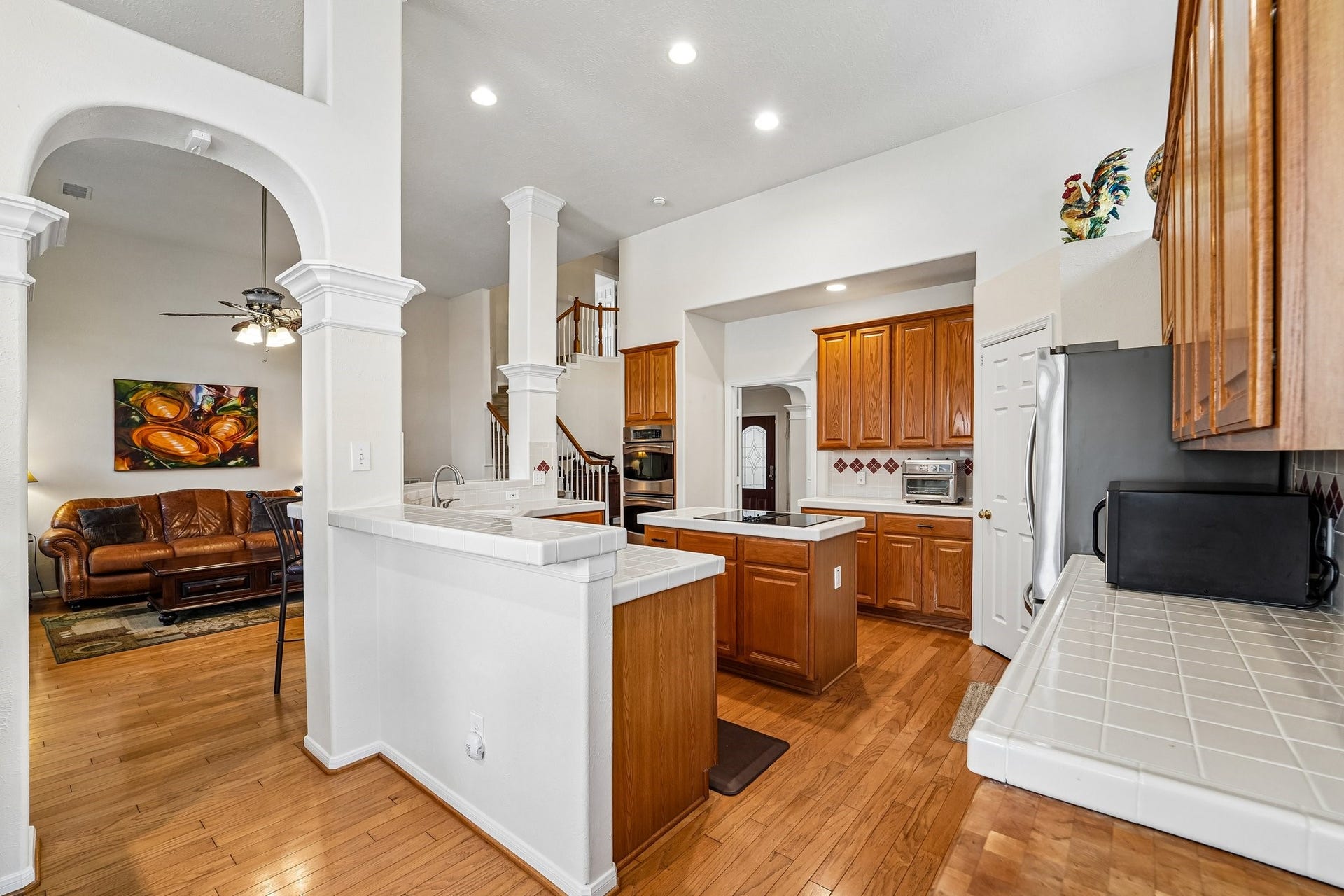14 Serene Creek Place, The Woodlands, TX 77382 Spacious kitchen with warm wood cabinetry, featuring a central island and stainless steel appliances, opens to a cozy living area with elegant archways and hardwood floors.