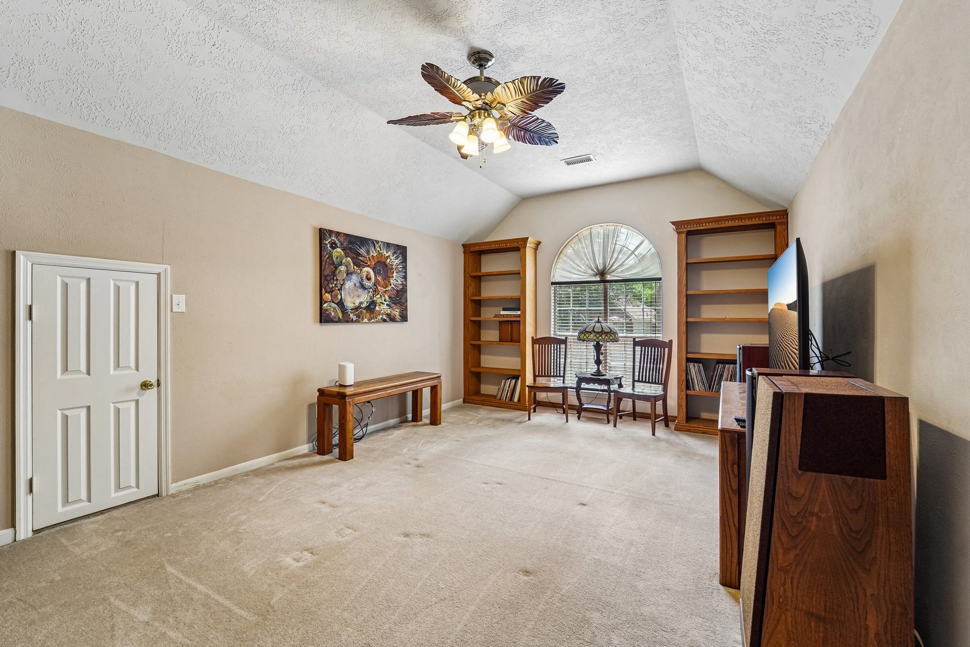 14 Serene Creek Place, The Woodlands, TX 77382 Spacious entertainment room with vaulted ceiling, featuring built-in bookshelves, a large arched window for natural light, and a ceiling fan.