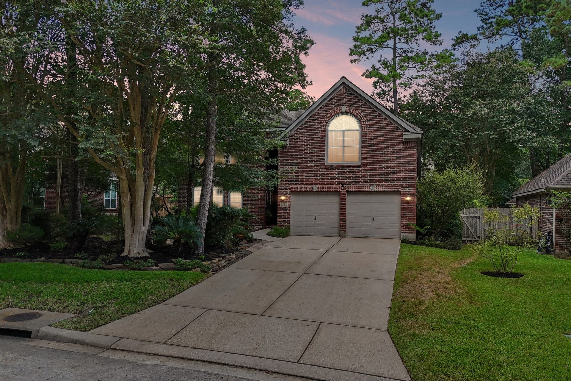 14 Serene Creek Place, The Woodlands, TX 77382 Charming brick home nestled among mature trees, featuring a spacious driveway and a two-car garage, offering a welcoming and serene atmosphere.
