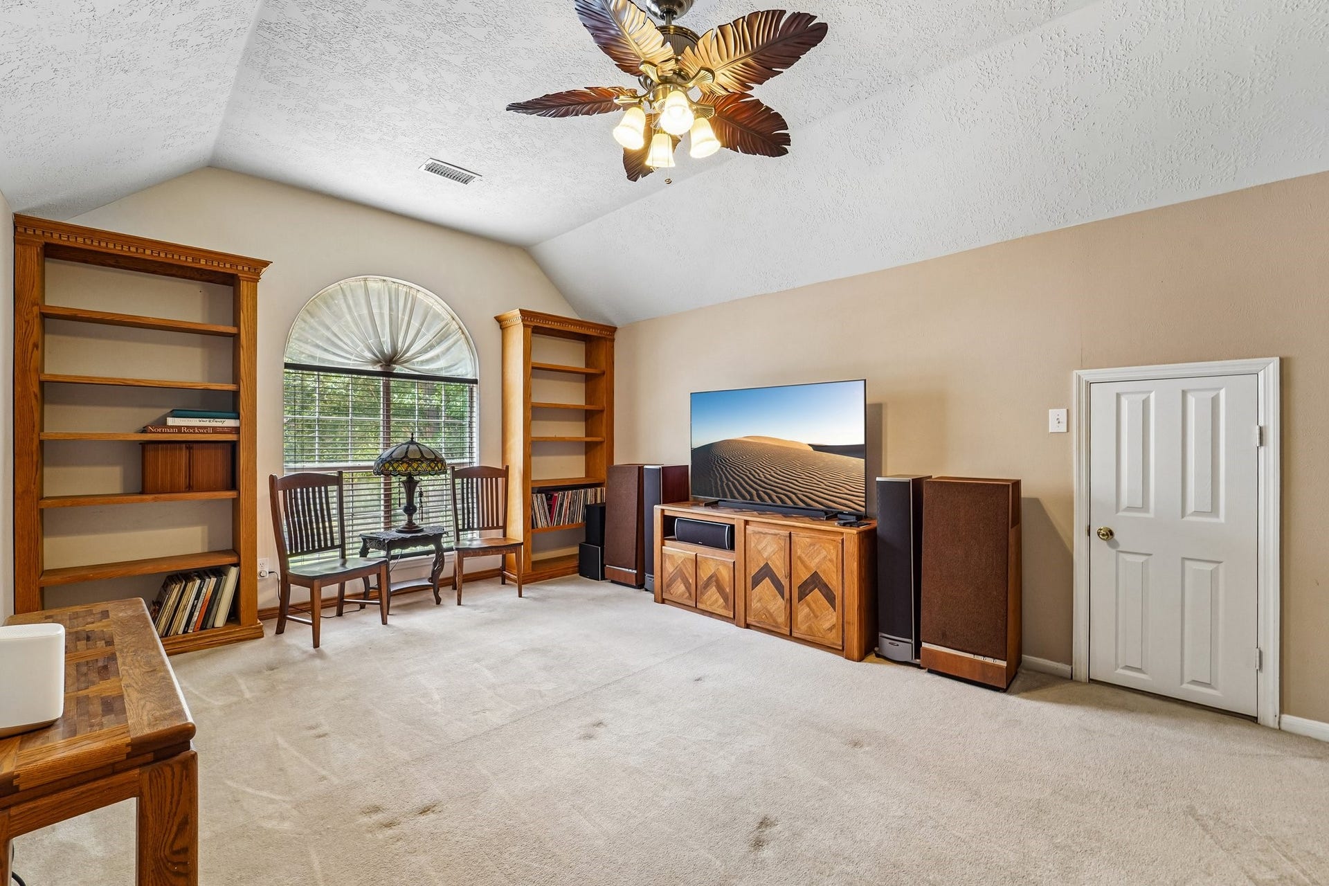 14 Serene Creek Place, The Woodlands, TX 77382 Spacious entertainment room featuring built-in bookshelves, a large window with an arched design, and ample space for seating and media equipment.