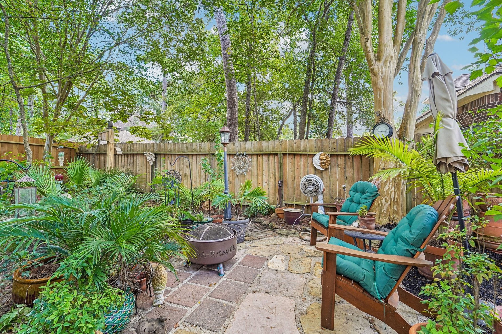 14 Serene Creek Place, The Woodlands, TX 77382 Charming and tranquil backyard oasis featuring lush greenery, cozy seating, and a rustic patio, perfect for relaxation and outdoor gatherings.