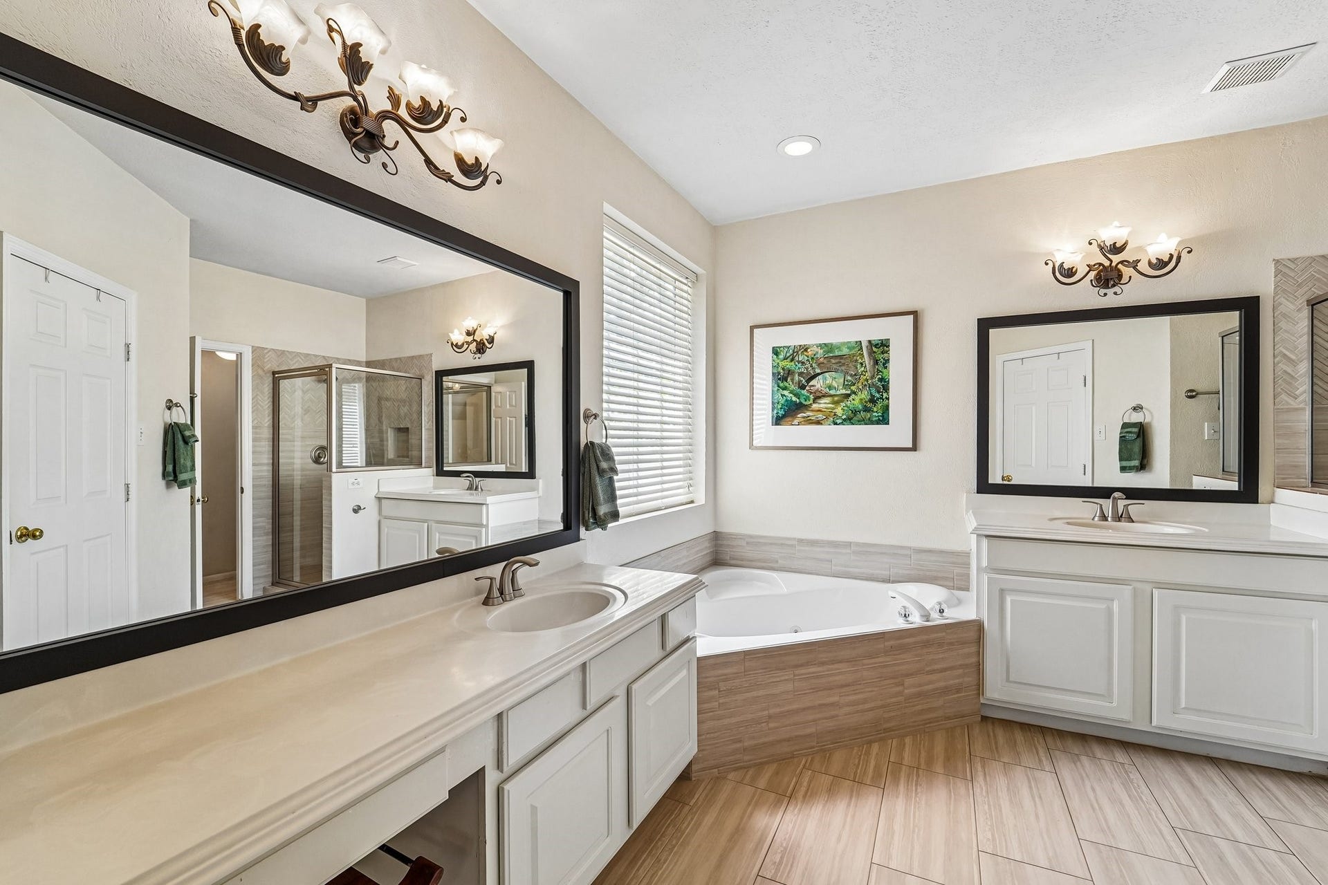 14 Serene Creek Place, The Woodlands, TX 77382 Primary bathroom features a luxurious corner bathtub, dual vanities with elegant lighting, and a large mirror, complemented by a separate glass-enclosed shower.
