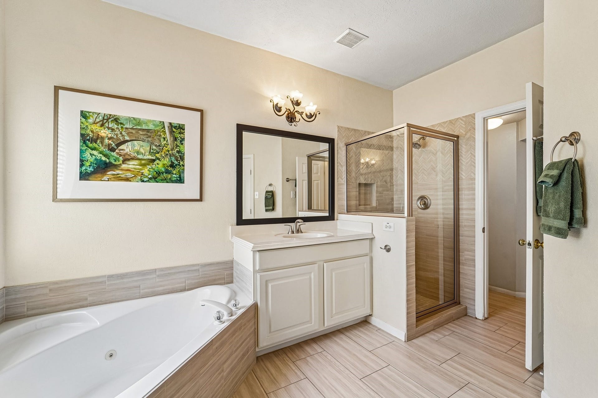 14 Serene Creek Place, The Woodlands, TX 77382 Primary bathroom features a luxurious corner bathtub, dual vanities with elegant lighting, and a large mirror, complemented by a separate glass-enclosed shower.