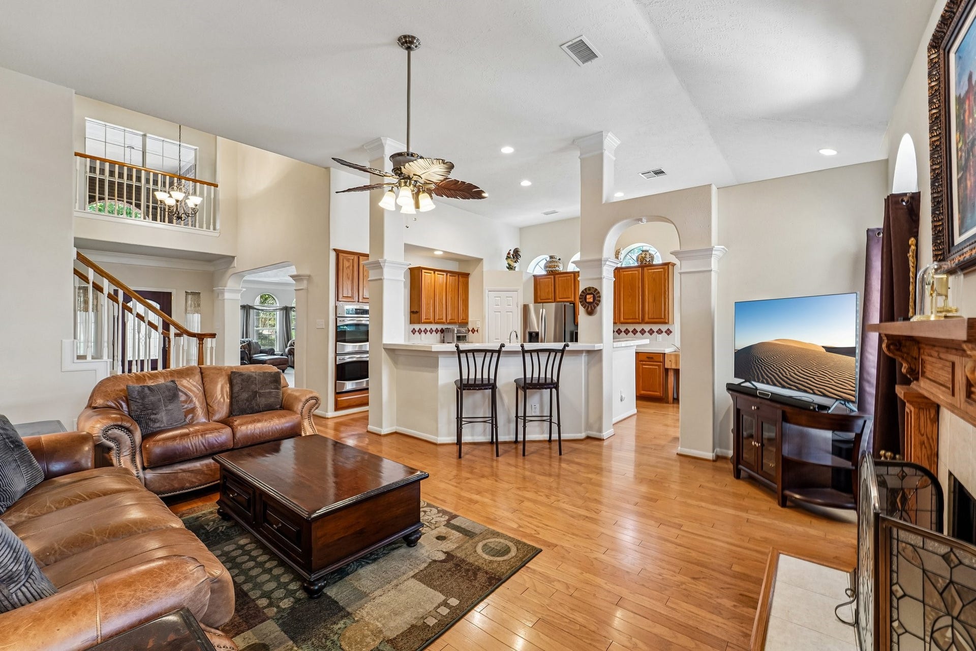 14 Serene Creek Place, The Woodlands, TX 77382 Spacious open-concept living area with high ceilings, featuring a cozy seating arrangement, elegant hardwood floors, and a stylish kitchen with a breakfast bar and separate breakfast room.