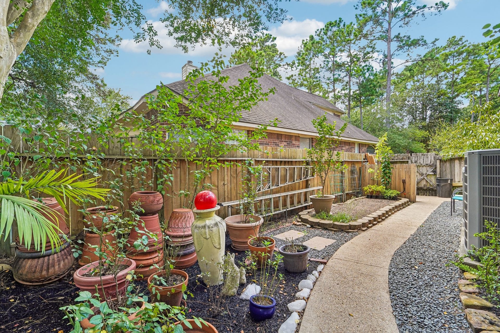 14 Serene Creek Place, The Woodlands, TX 77382 Charming backyard oasis with lush greenery, decorative planters, and a curved path leading to a cozy seating area, perfect for relaxation and outdoor enjoyment.