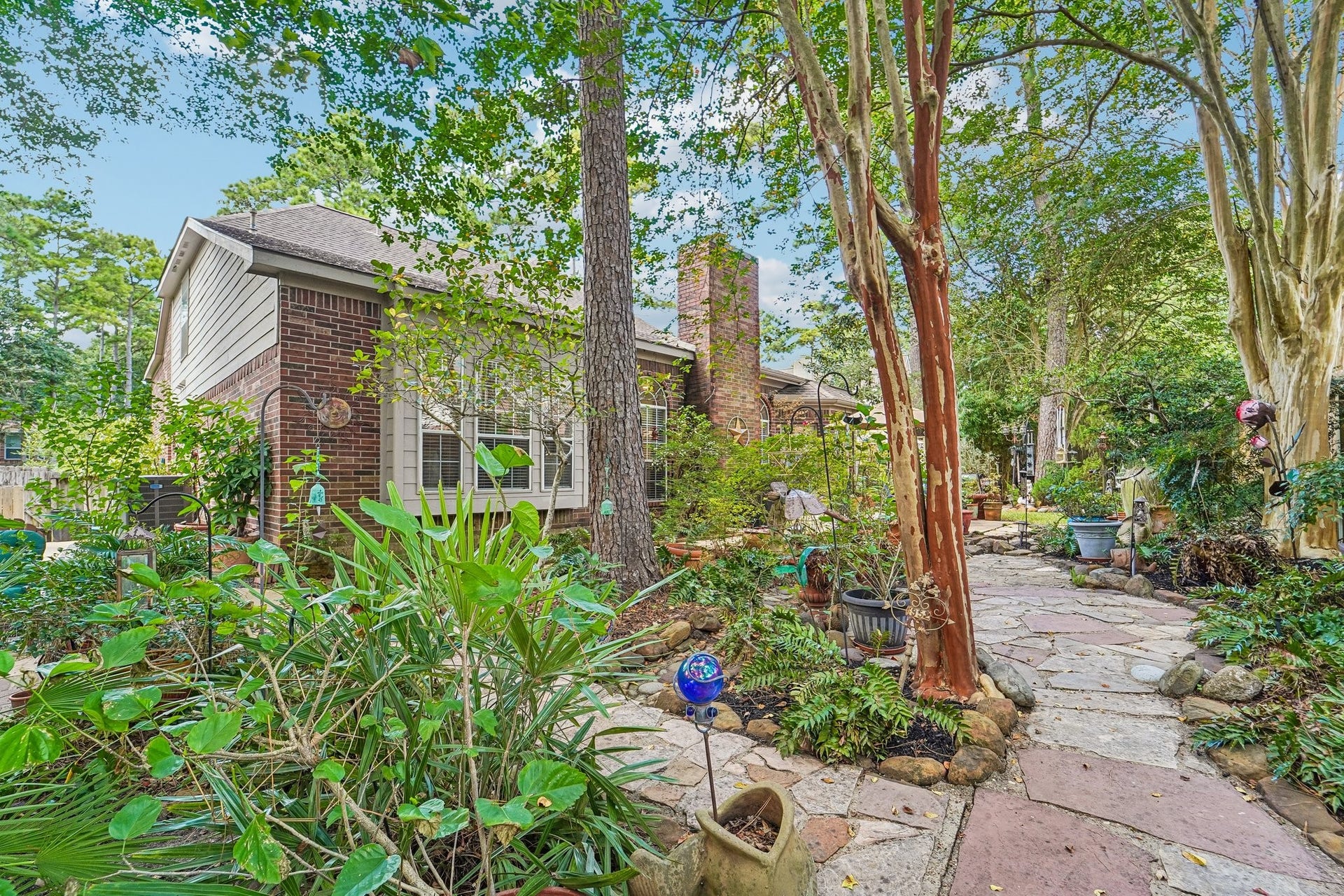 14 Serene Creek Place, The Woodlands, TX 77382 Charming home with a lush, landscaped garden featuring a stone pathway, mature trees, and vibrant greenery, creating a serene outdoor retreat.