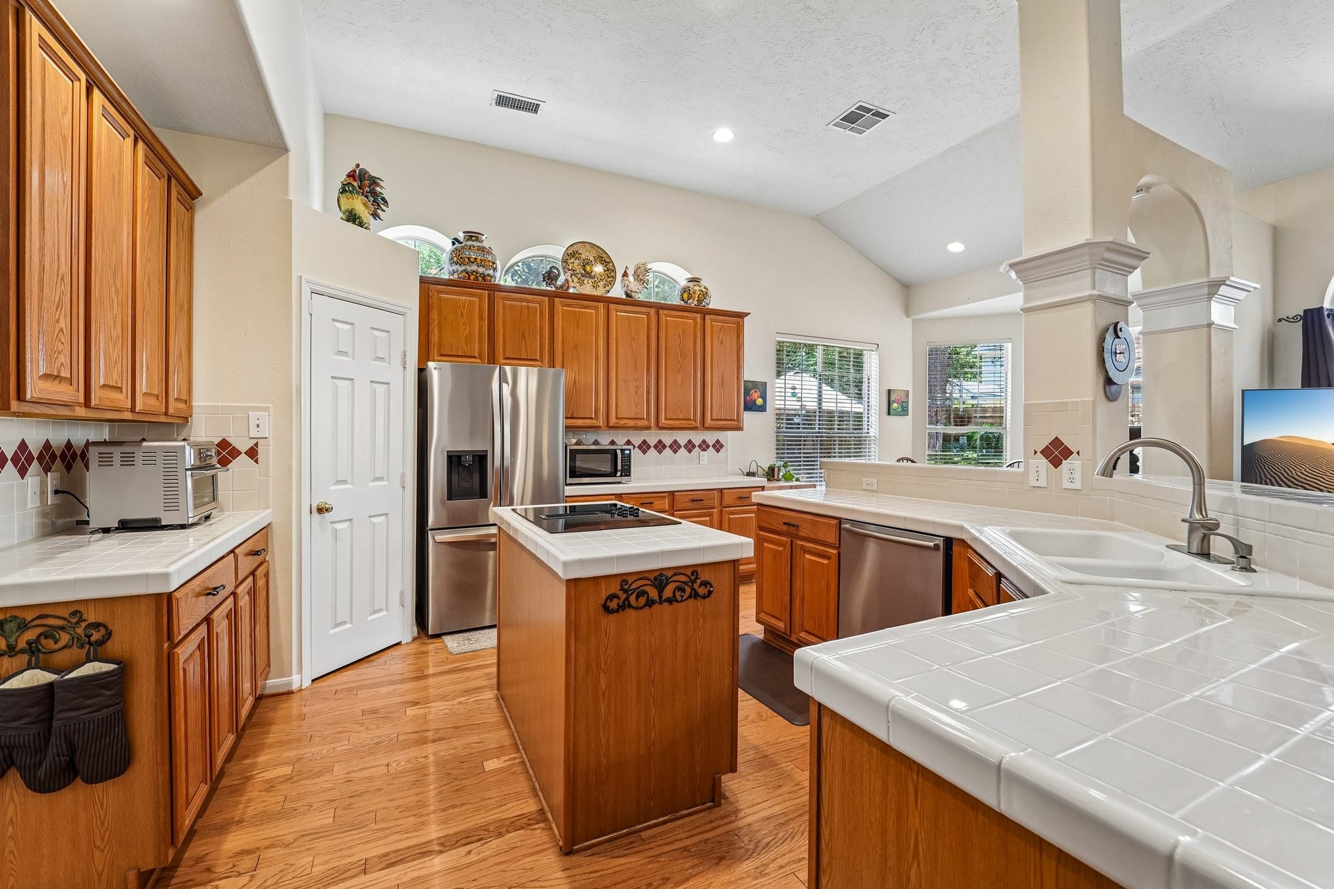 14 Serene Creek Place, The Woodlands, TX 77382 Spacious kitchen featuring warm wood cabinetry, stainless steel appliances, and a central island, complemented by ample natural light and elegant tile accents.