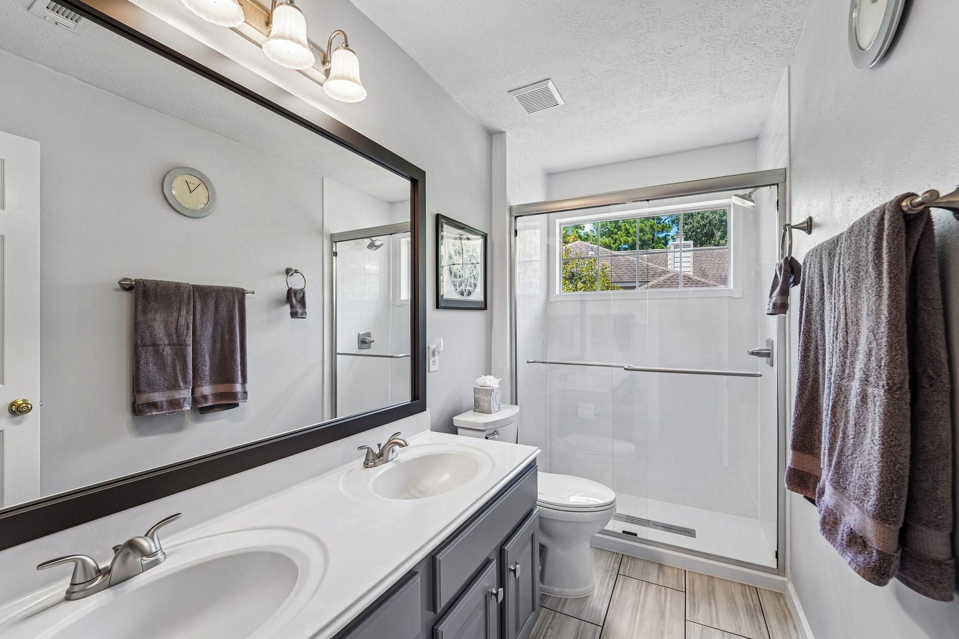 14 Serene Creek Place, The Woodlands, TX 77382 Bright and updated bathroom featuring a dual-sink vanity, large mirror, and a spacious glass-enclosed shower, complemented by natural light from a sizable window.