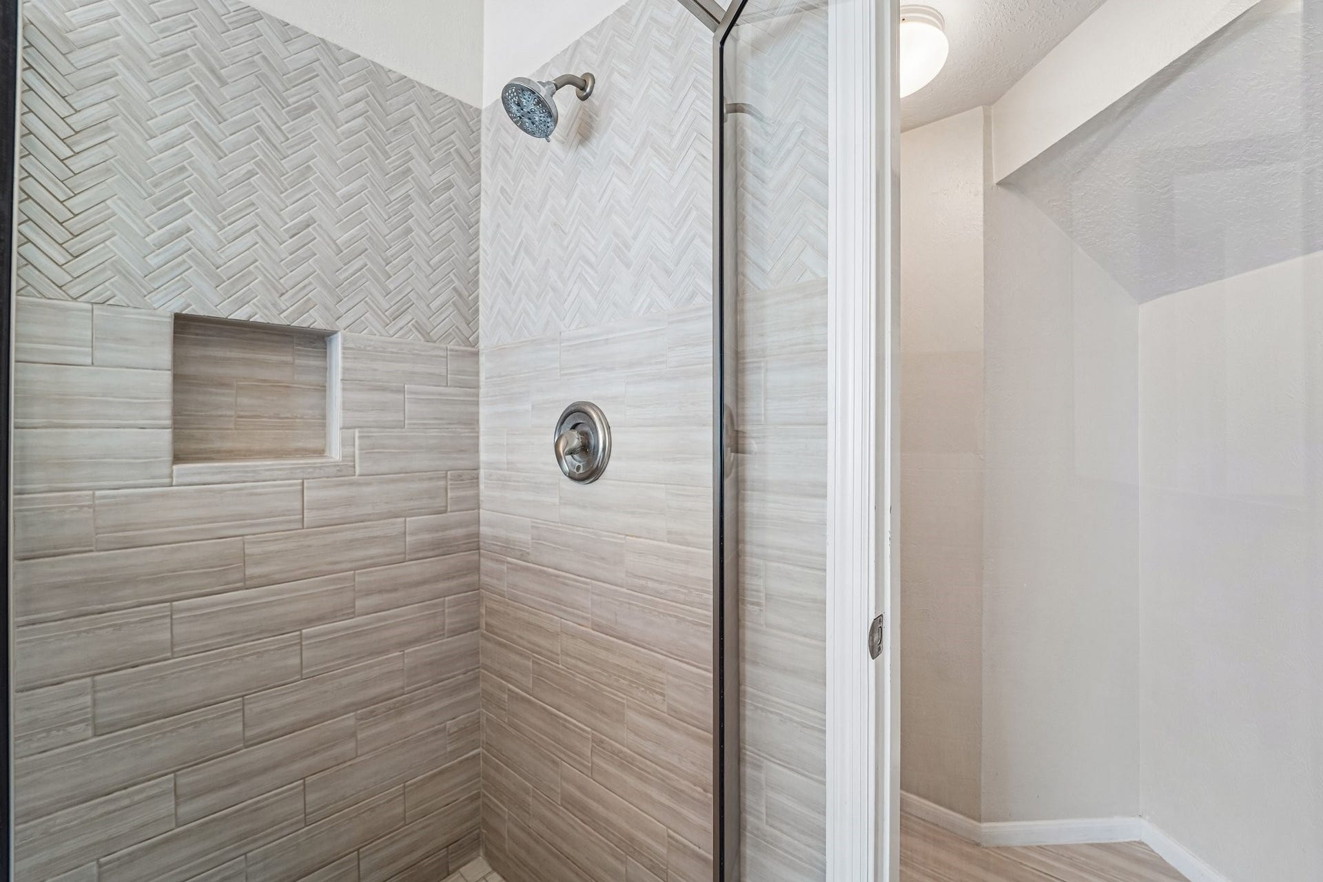 14 Serene Creek Place, The Woodlands, TX 77382 Close up view of the remodeled shower in the primary bath. Features stylish herringbone and subway tile design with built-in niche.