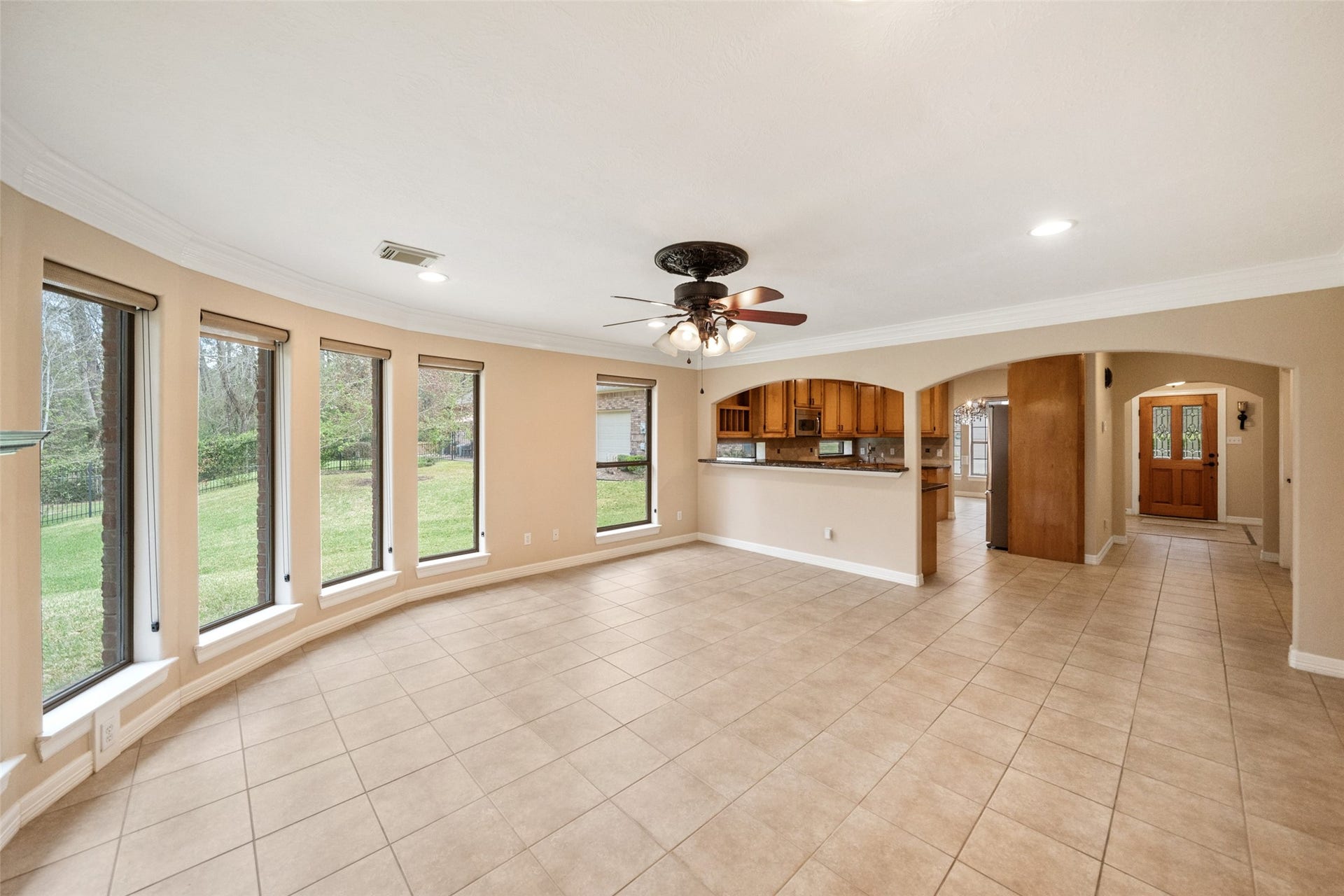901 Longmire Road, #28, Conroe, TX 77304 This spacious living area features large windows for ample natural light, a ceiling fan, and tiled flooring. It opens to a kitchen with wooden cabinetry and a convenient passthrough, creating a seamless flow.