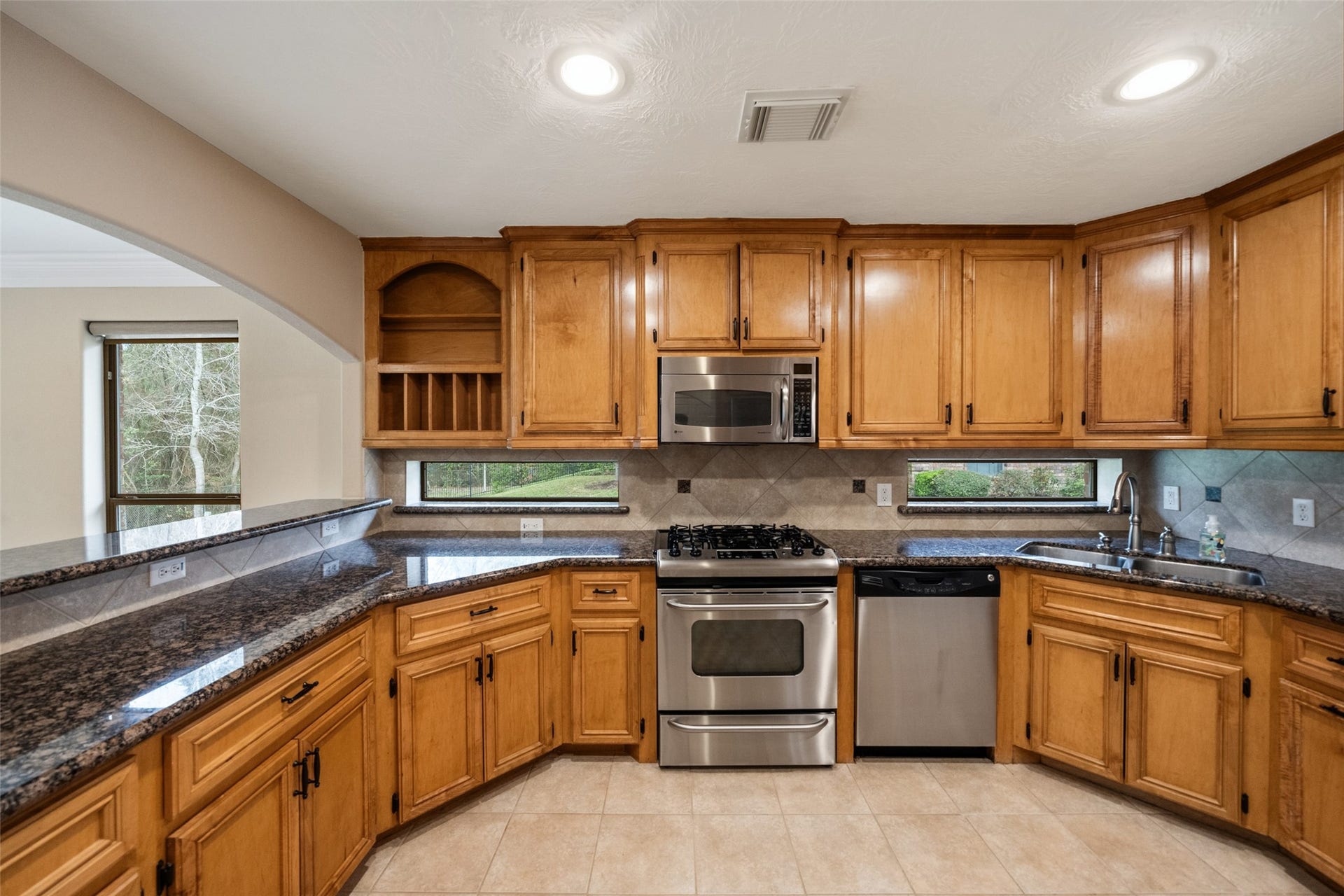 901 Longmire Road, #28, Conroe, TX 77304 This kitchen features warm wood cabinetry, granite countertops, and stainless steel appliances, including a gas stove and dishwasher. It has a cozy corner sink with a window view, ample storage, and a tile backsplash, creating a functional and inviting space.