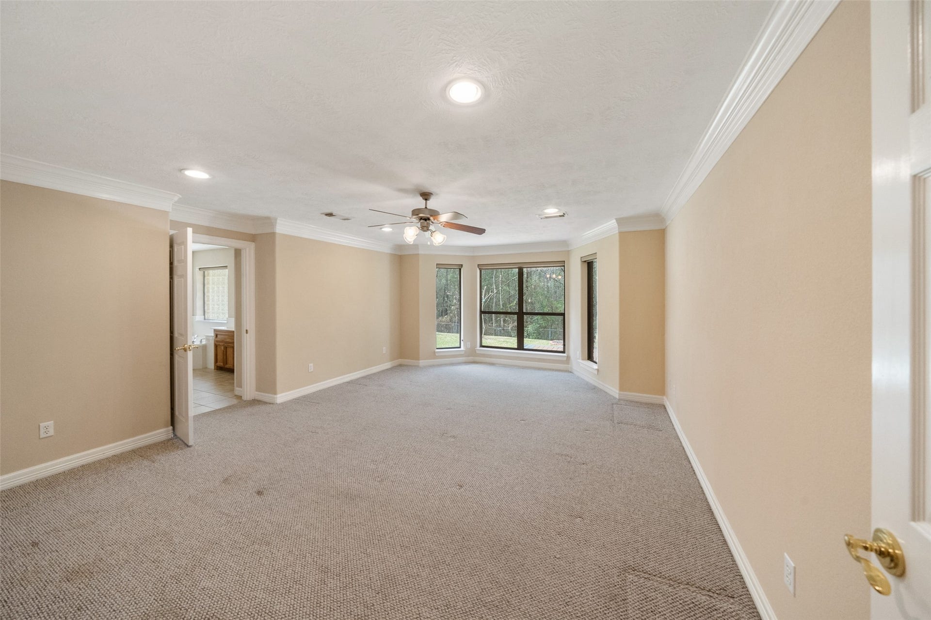 901 Longmire Road, #28, Conroe, TX 77304 Spacious primary bedroom with crown molding. Features recessed lighting, ceiling fan, and large windows offering natural light. Adjacent to a bathroom with visible vanity area.