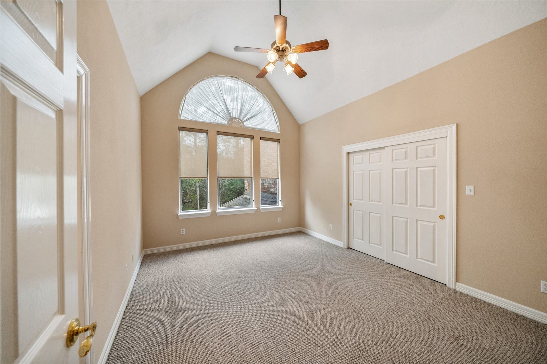 901 Longmire Road, #28, Conroe, TX 77304 Upstairs secondary bedroom features a vaulted ceiling with a fan, a large arched window providing natural light, neutral walls, and carpeted flooring. It includes a spacious closet with double doors with ensuite bathroom.